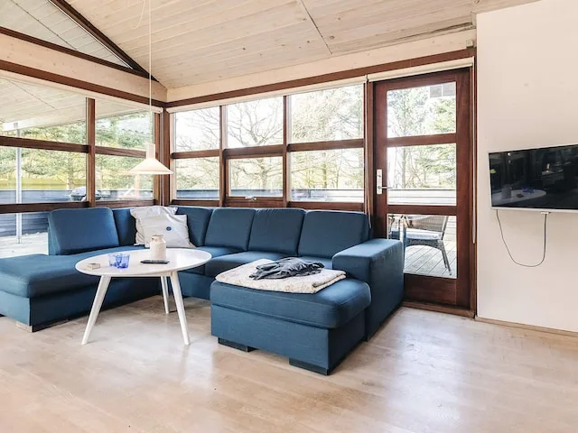 A bright living room with blue seating, large windows, and a wall-mounted television.