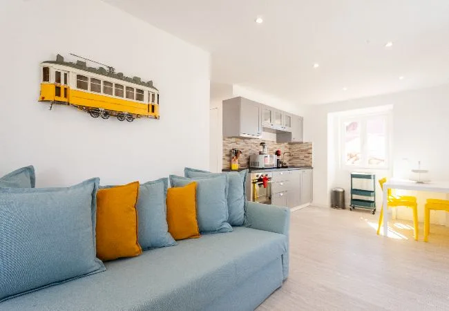Una luminosa sala de estar con asientos azules junto a una cocina abierta y una mesa de comedor.
