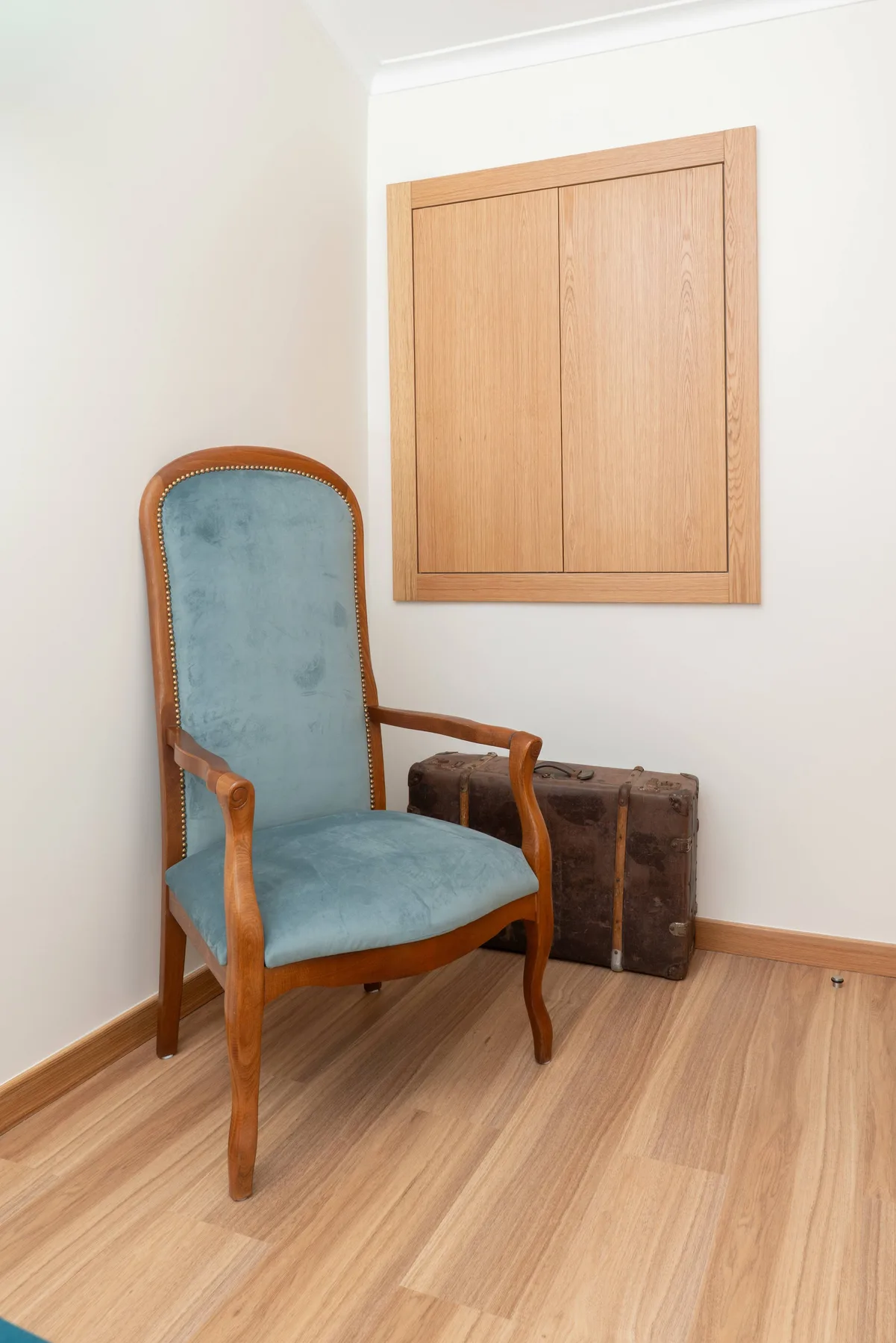 Una silla tapizada azul está debajo de un panel de madera en una habitación luminosa.