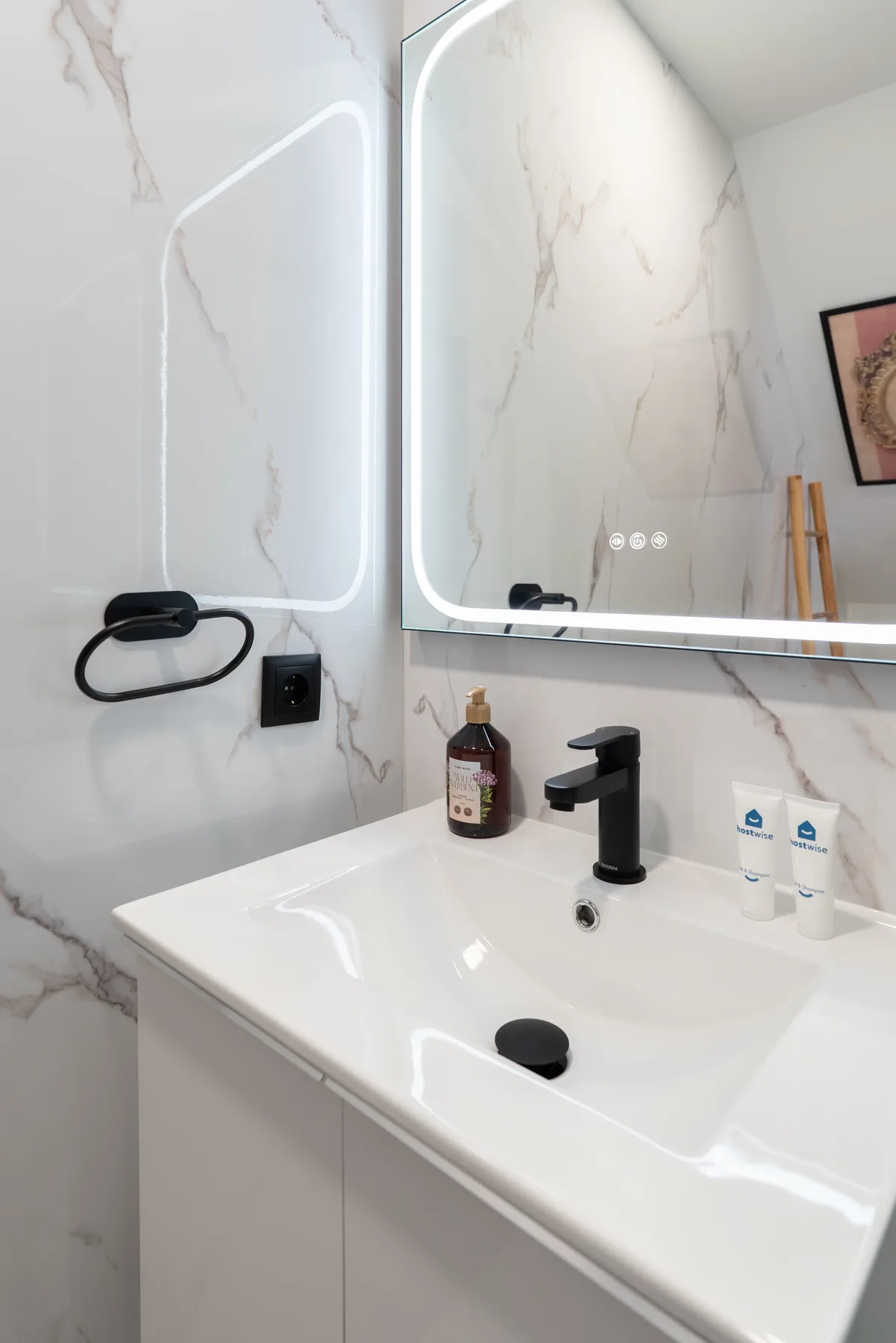 Un lavabo de baño con grifo oscuro y espejo iluminado.