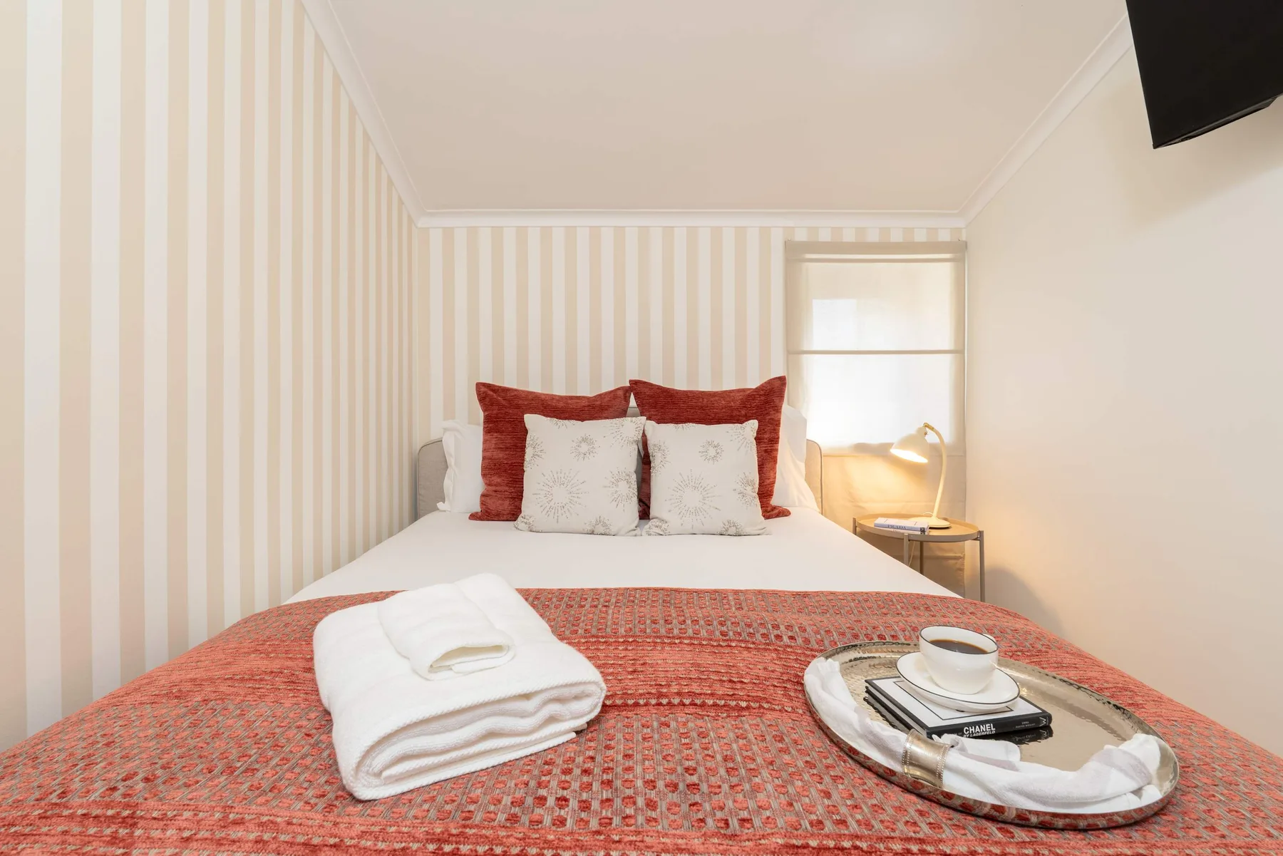 Un dormitorio con una cama bien arreglada, toallas dobladas y una lámpara de noche.