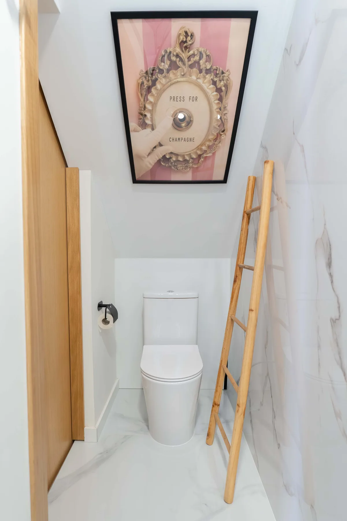 Un baño compacto con un inodoro, un cuadro enmarcado y una escalera de madera.