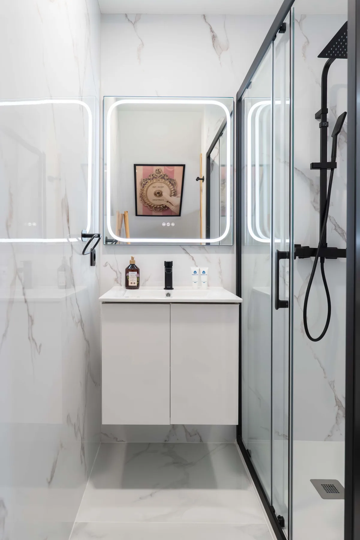 Baño luminoso con una ducha de vidrio y un lavabo bajo un cuadro enmarcado.