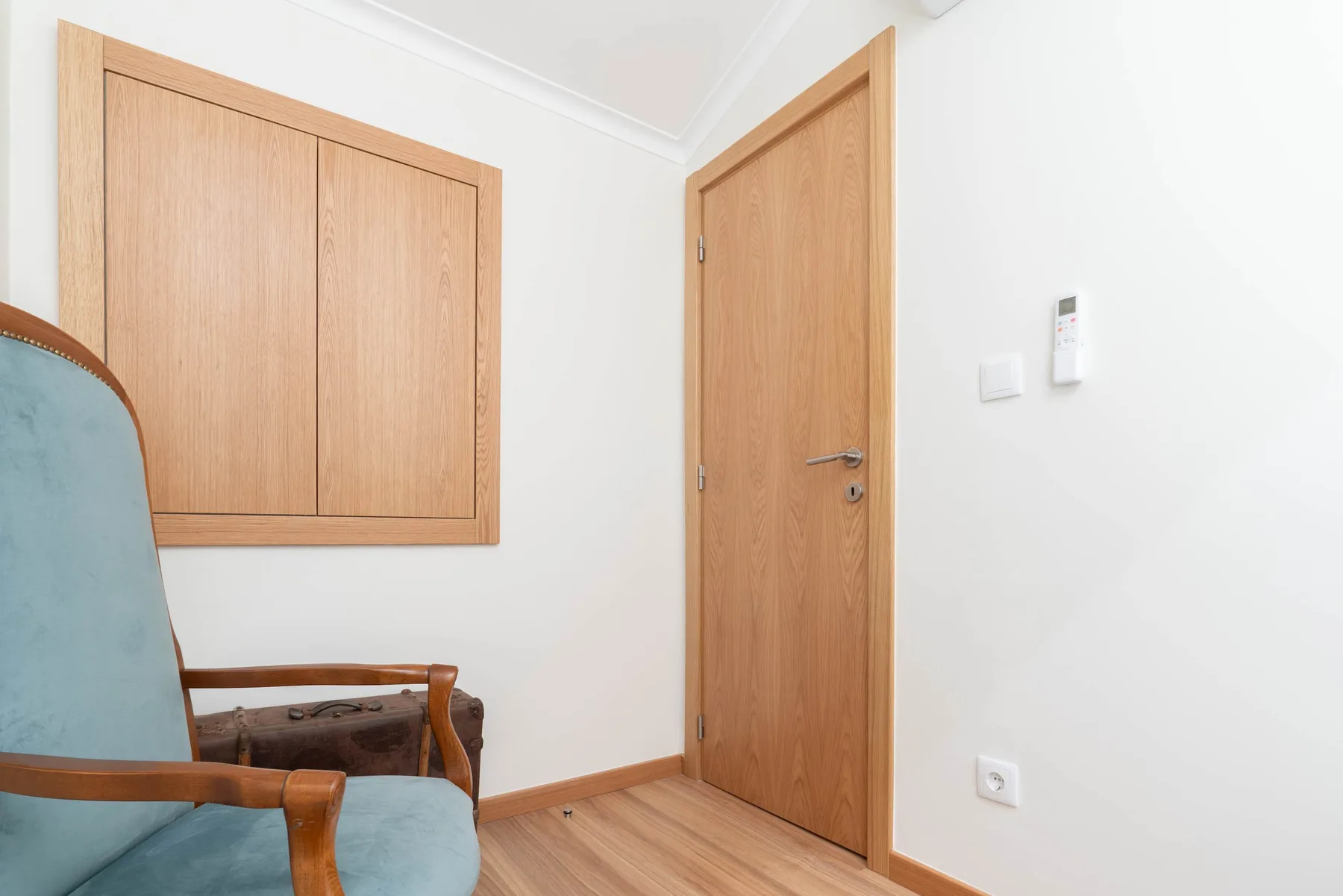 Una esquina de habitación con puertas de madera, paredes blancas y un asiento tapizado azul.