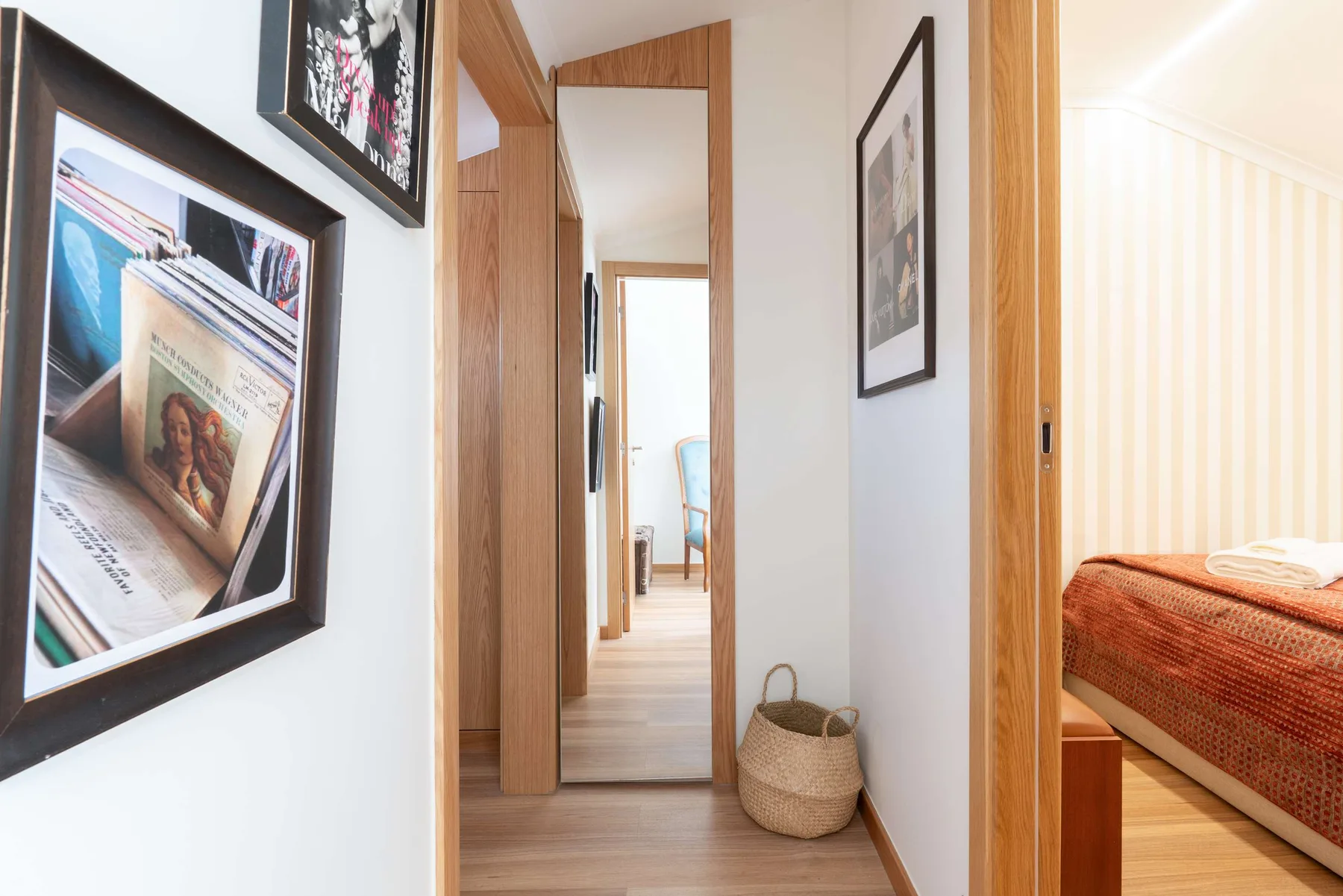 Un pasillo luminoso con cuadros enmarcados y una puerta abierta a un dormitorio.