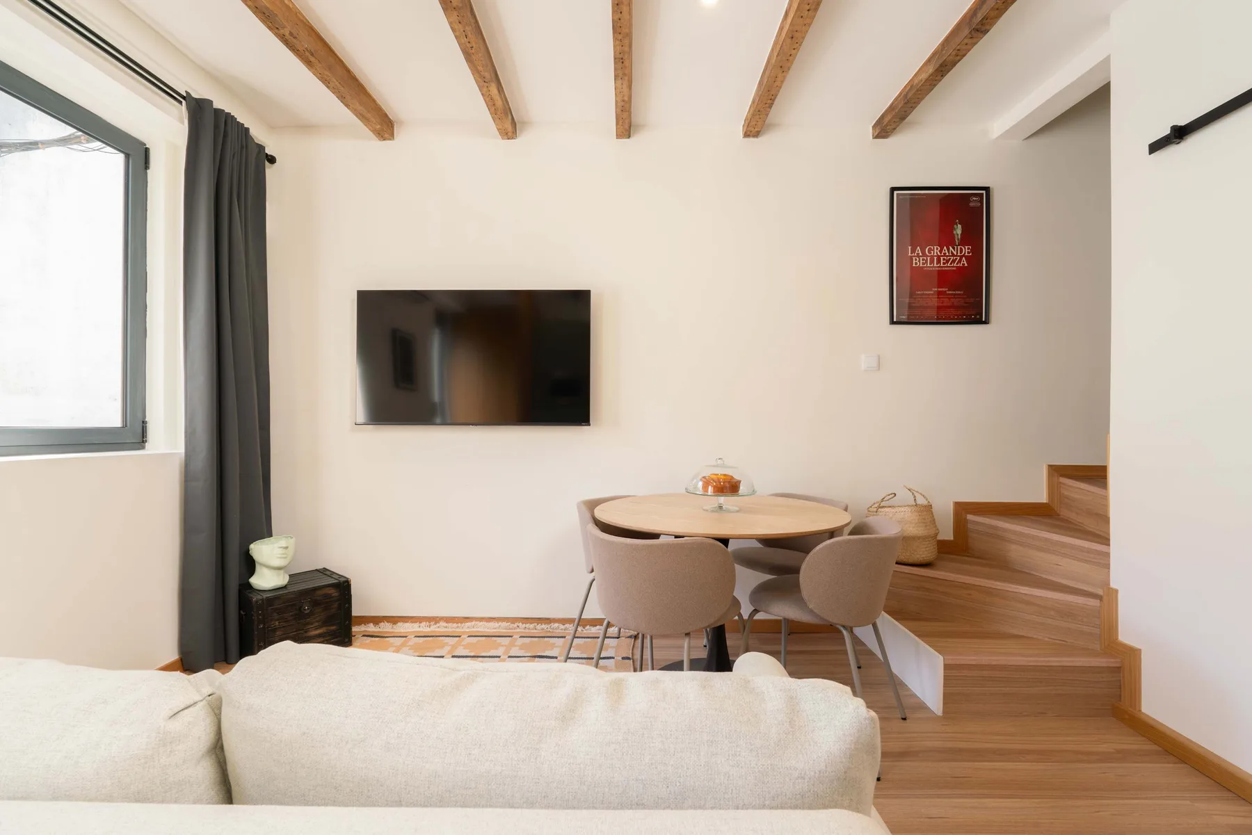 Una zona de estar y comedor con televisor en la pared y escalera de madera.