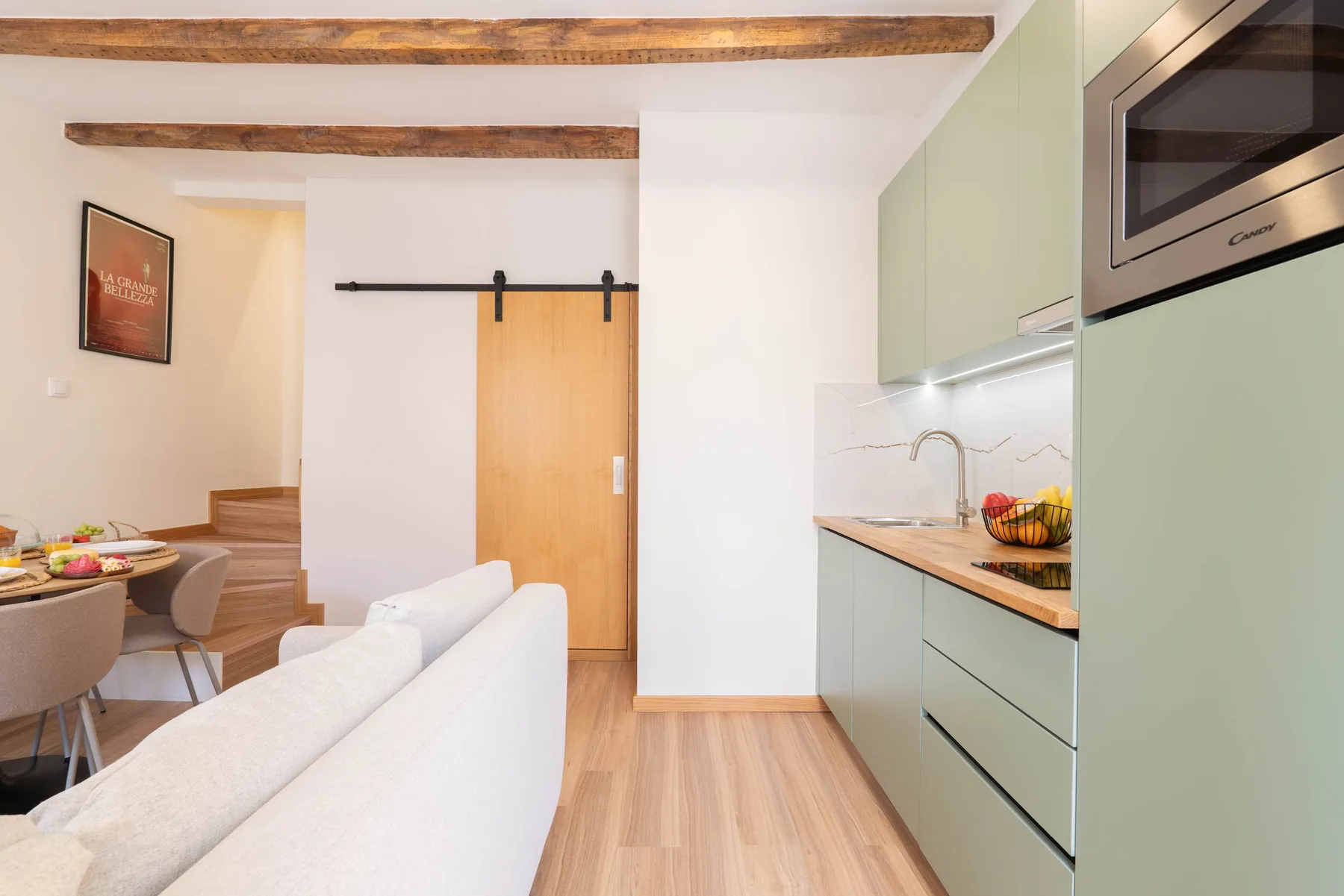 Una sala luminosa se abre a una cocina compacta con gabinetes verde claro.