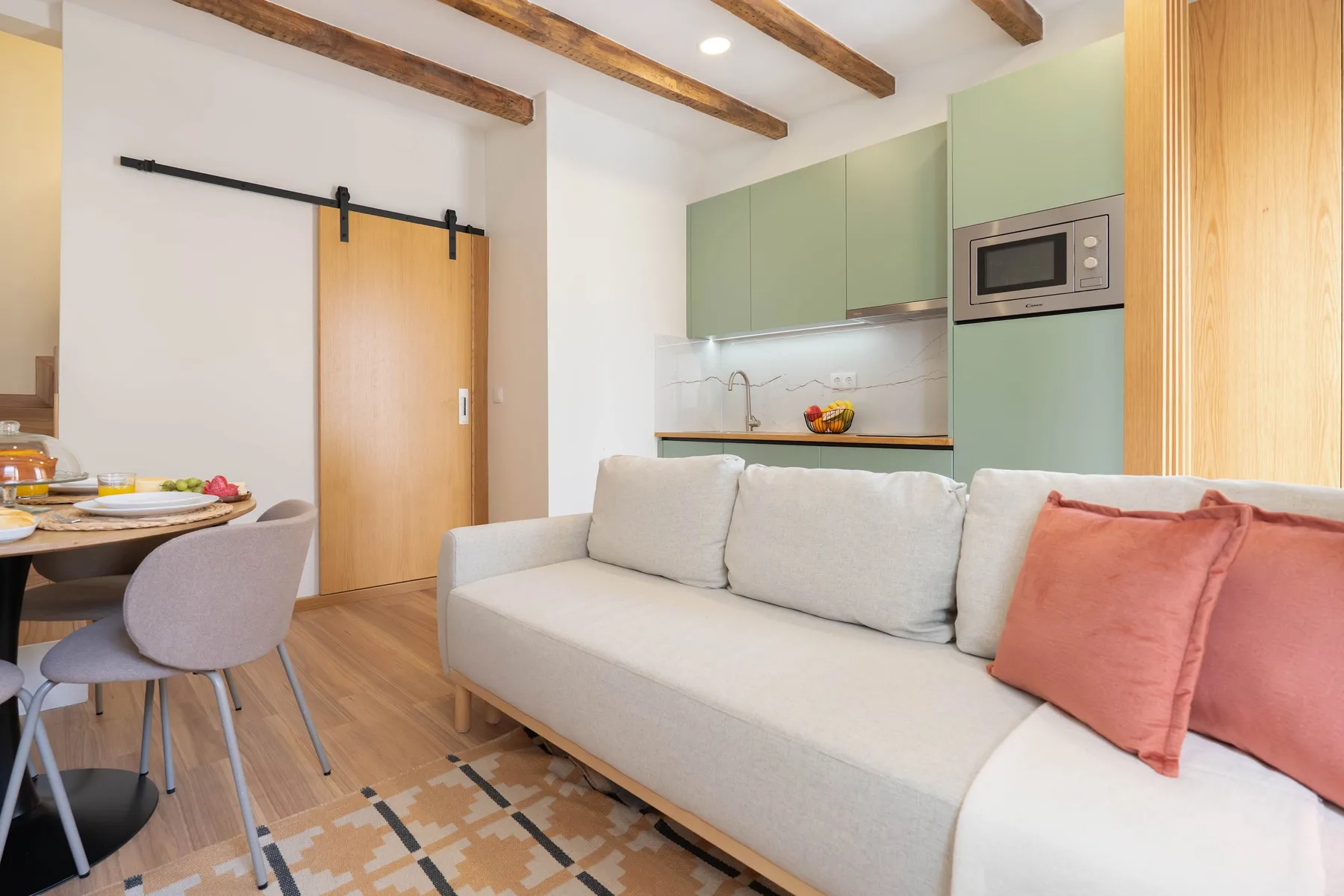 Una luminosa sala de estar con un sofá claro y una cocina compacta detrás.