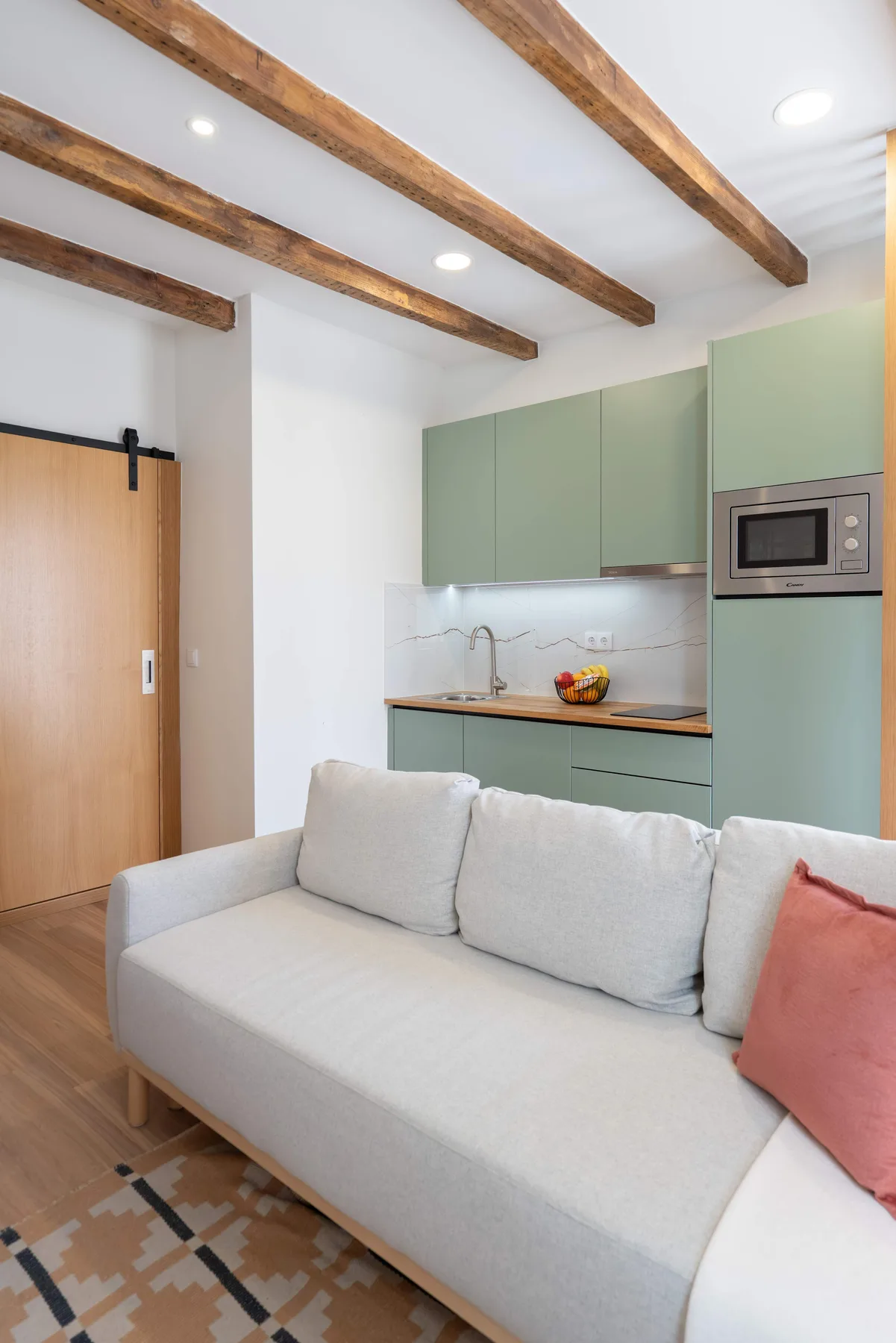 Una sala de estar con asientos claros frente a una cocina verde menta.