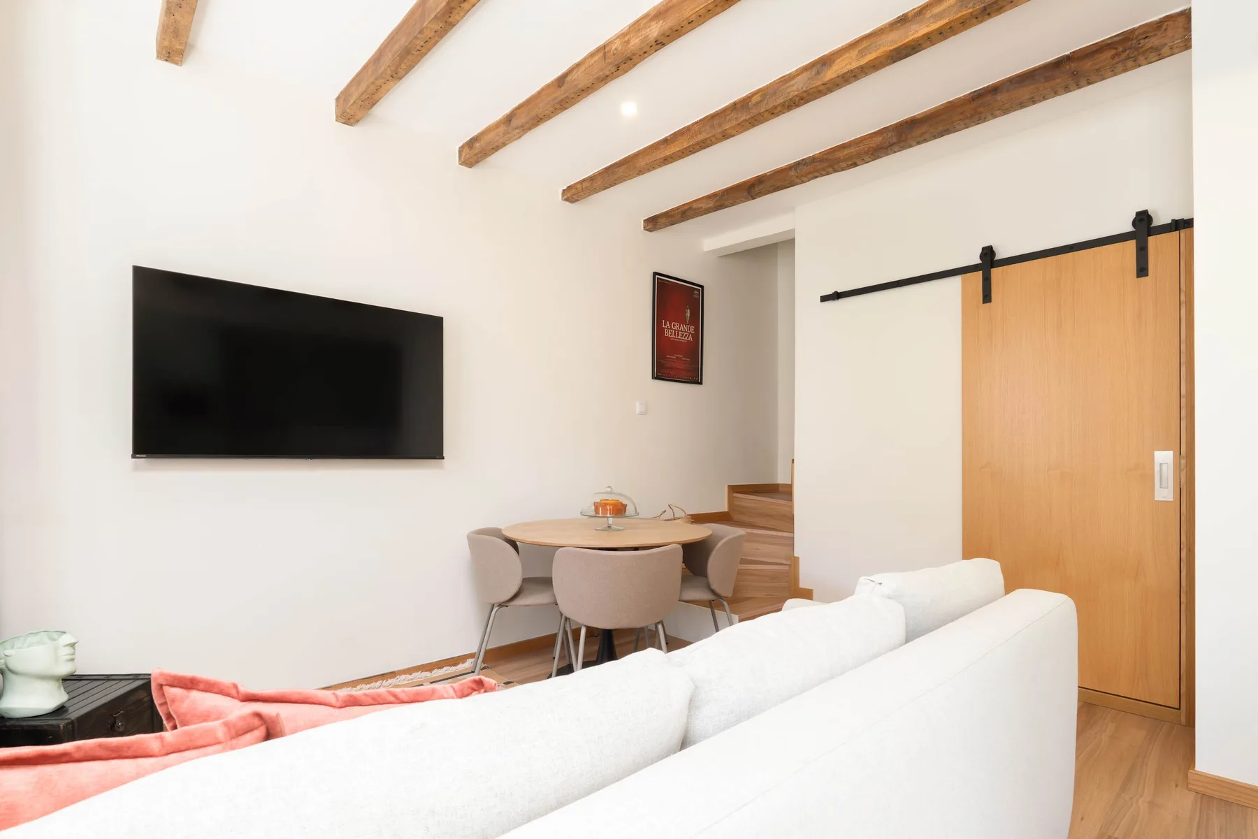Una sala de estar con asientos blancos, un televisor en la pared y una mesa de comedor.