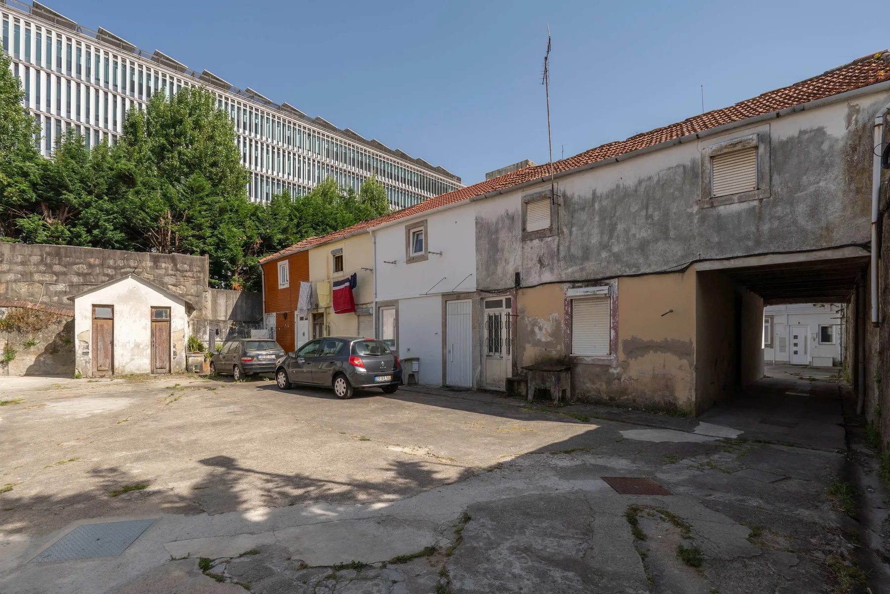 Zona común: Un patio exterior con coches aparcados y una hilera de edificios desgastados.
