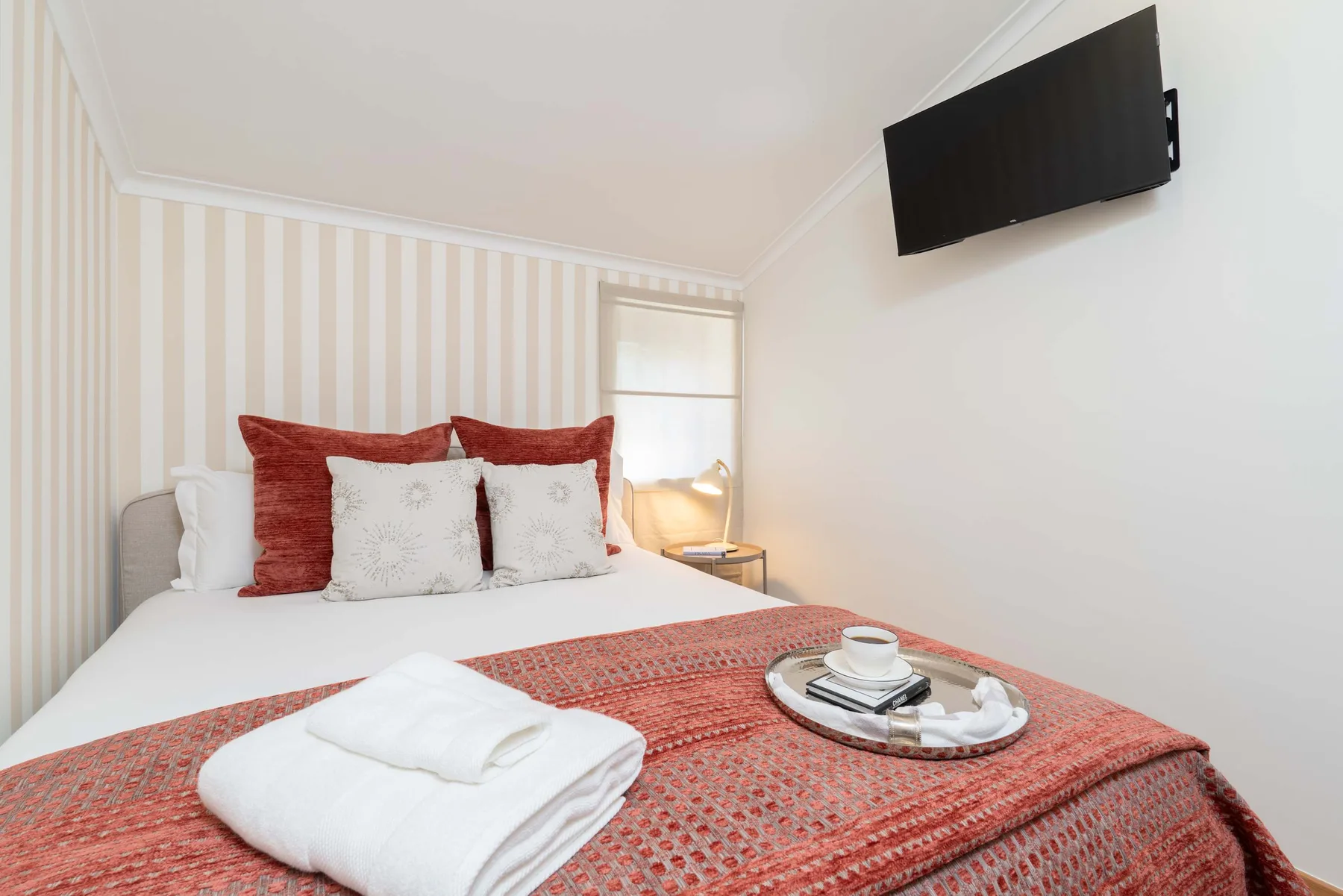Un dormitorio con una cama, toallas dobladas y un televisor montado en la pared.