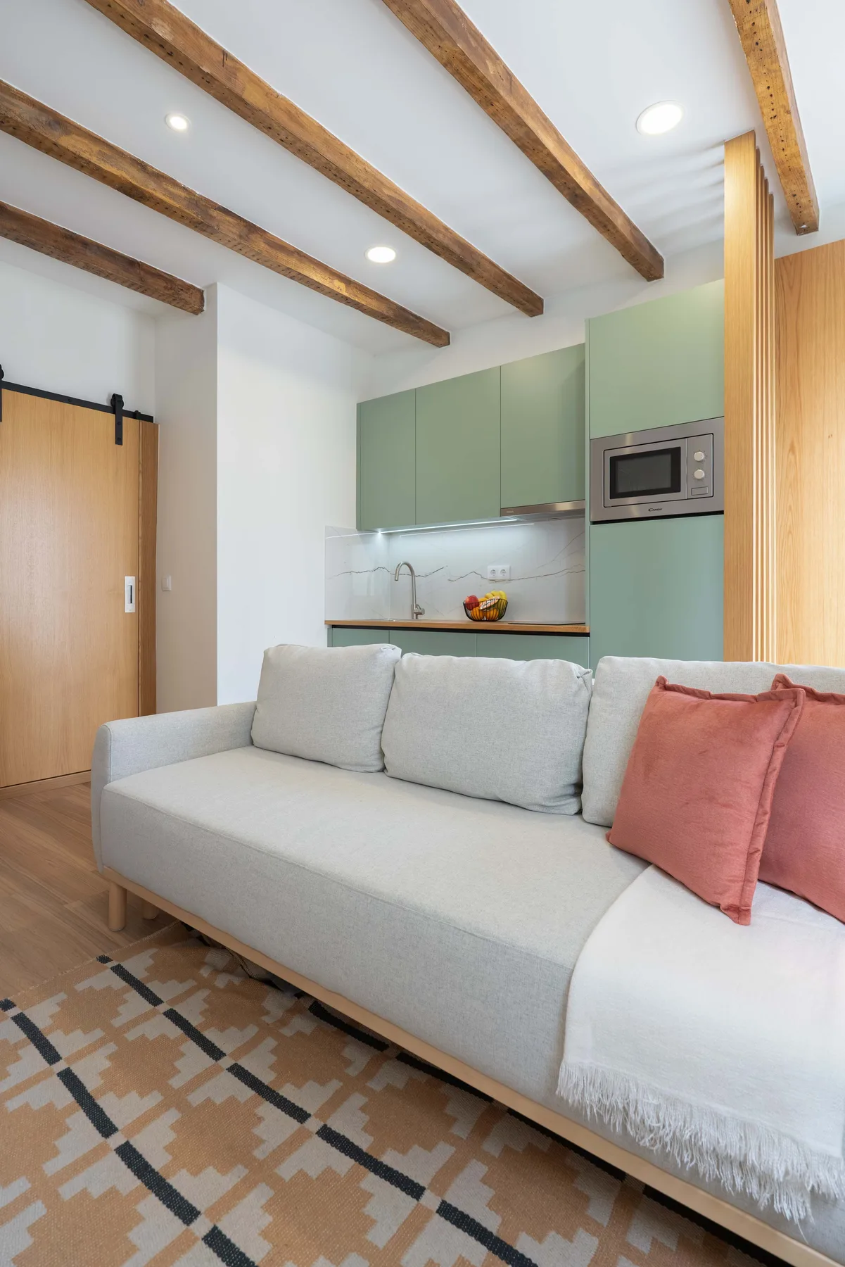 Una pequeña sala de estar con un sofá claro y una cocina verde al fondo.