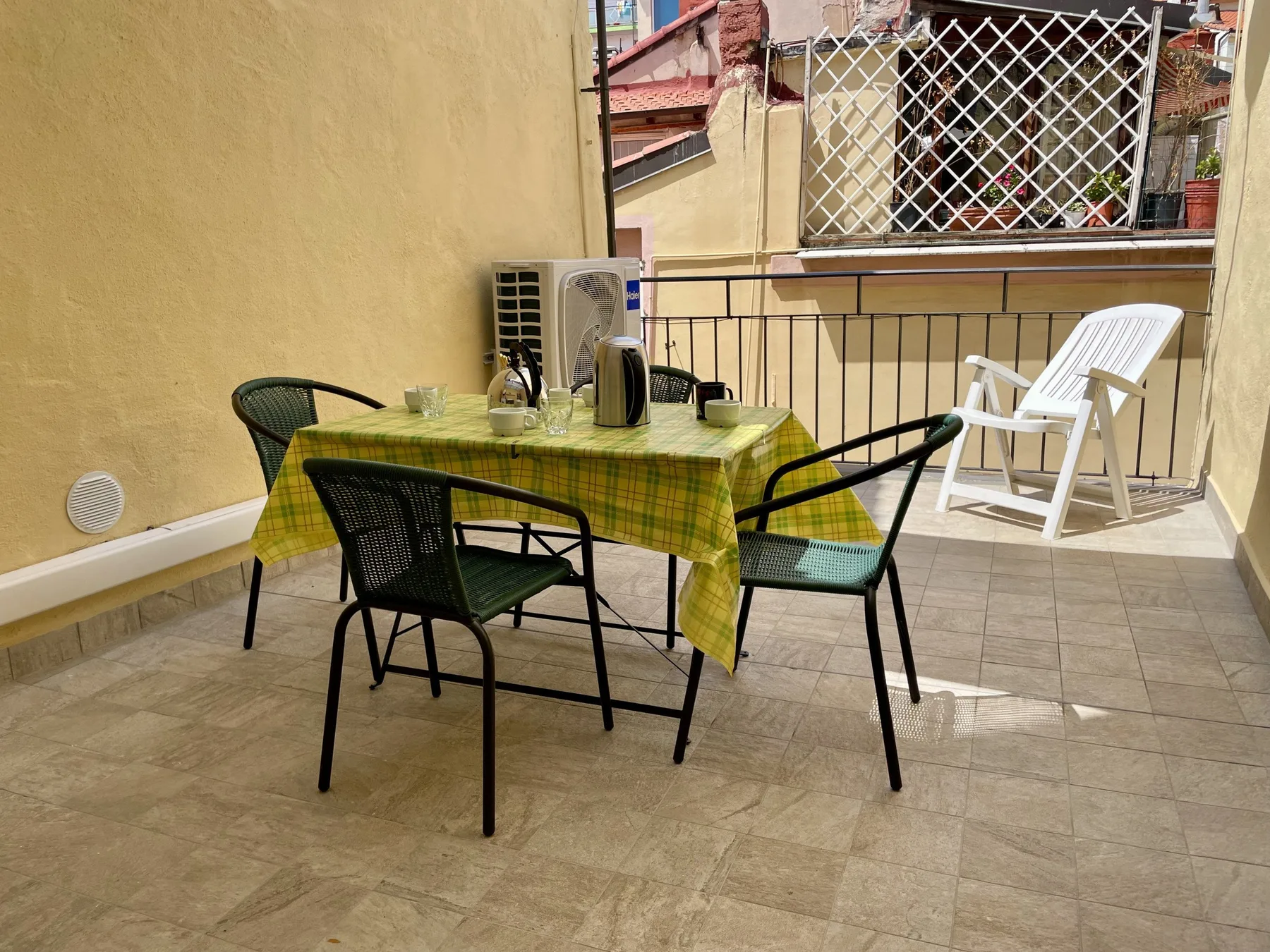 A sunny terrace with a dining table and chairs beside a white lounge chair.