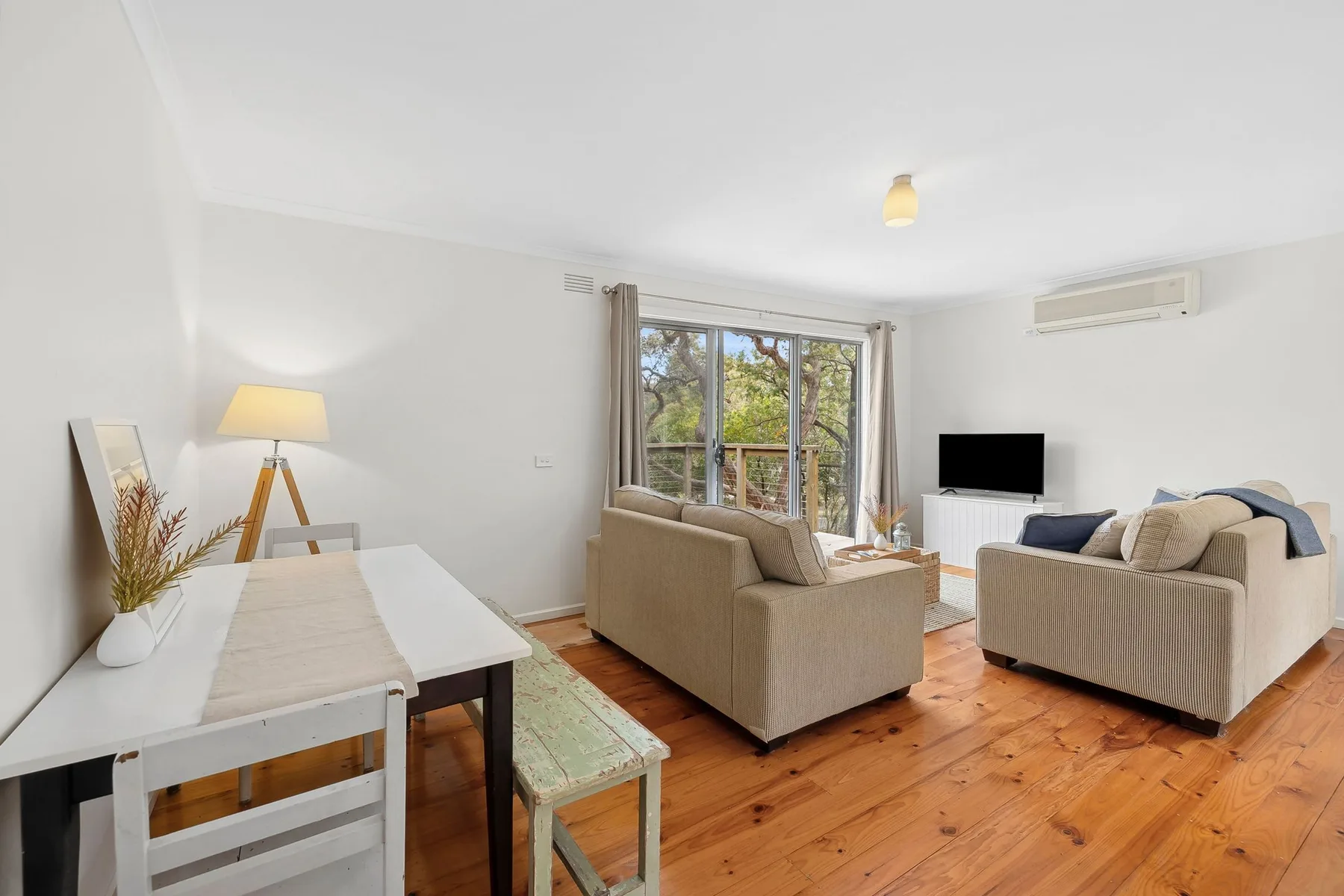 Una sala luminosa con asientos, un televisor y puertas de vidrio que dan a un balcón.