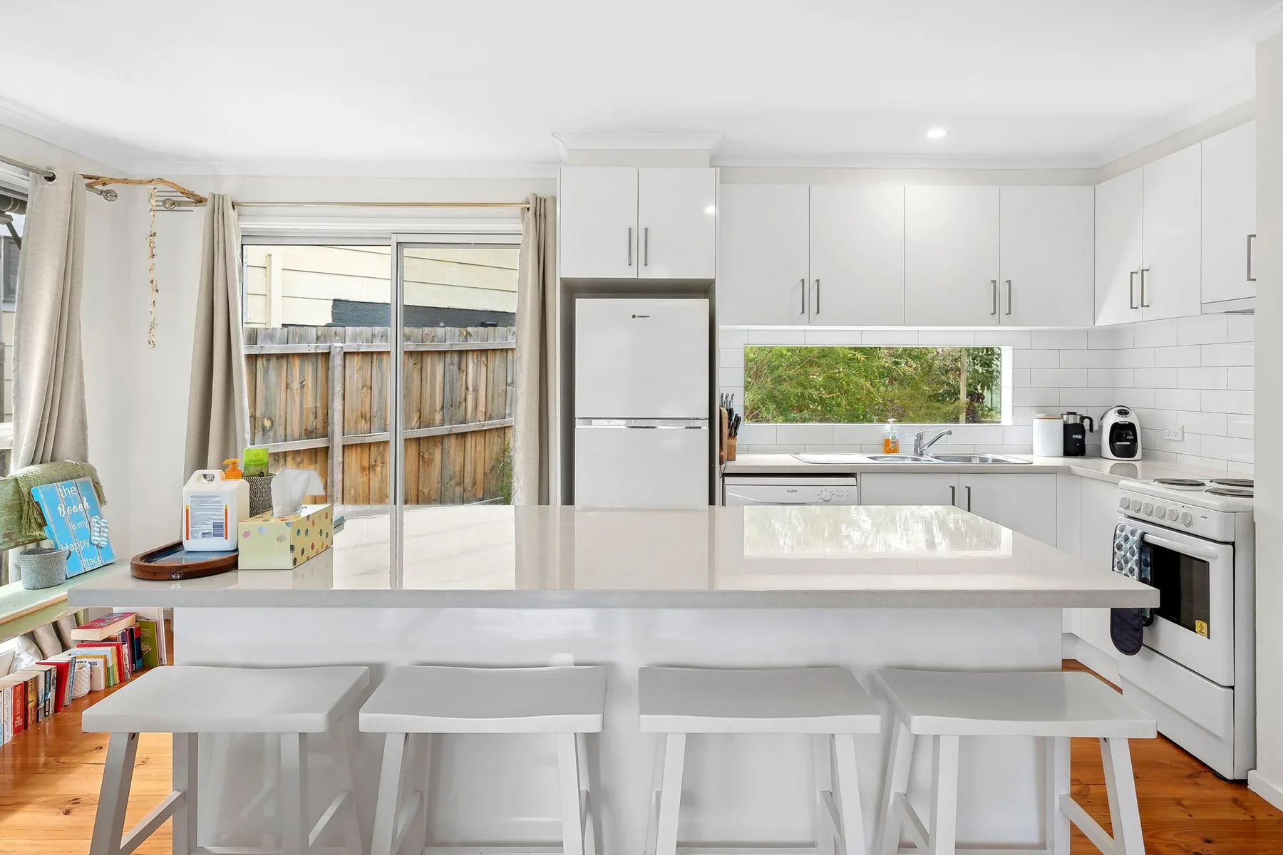 Una cocina luminosa con gabinetes blancos, una isla central y taburetes.