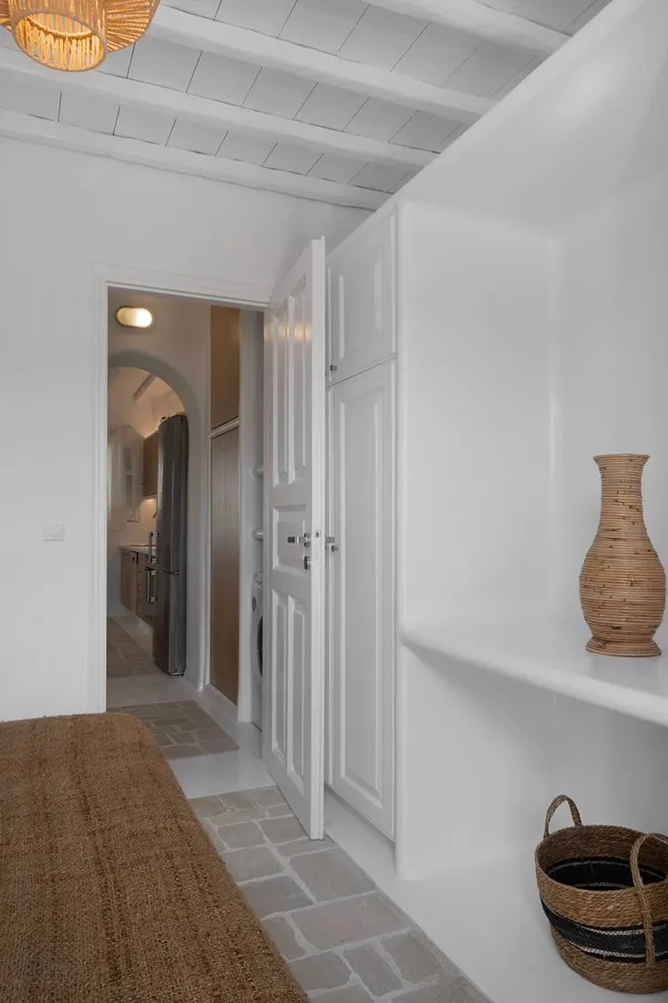 Un pasillo blanco y luminoso con puertas paneladas, suelo de piedra y decoración tejida.