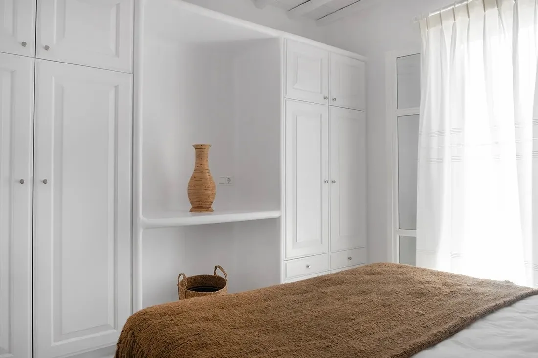 Un dormitorio con armarios blancos empotrados, un estante y una cama con una colcha marrón.