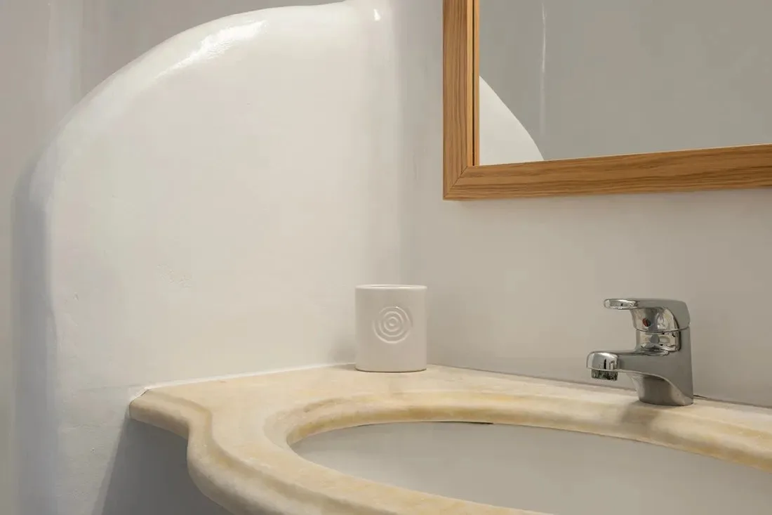 Un lavabo de baño con una pila curva y un espejo enmarcado.