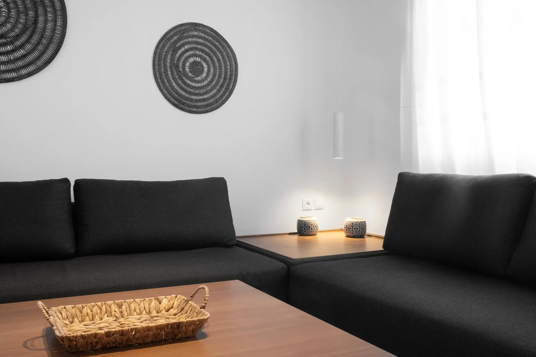 Una sala de estar con asientos oscuros, una mesa de madera y adornos tejidos en la pared.