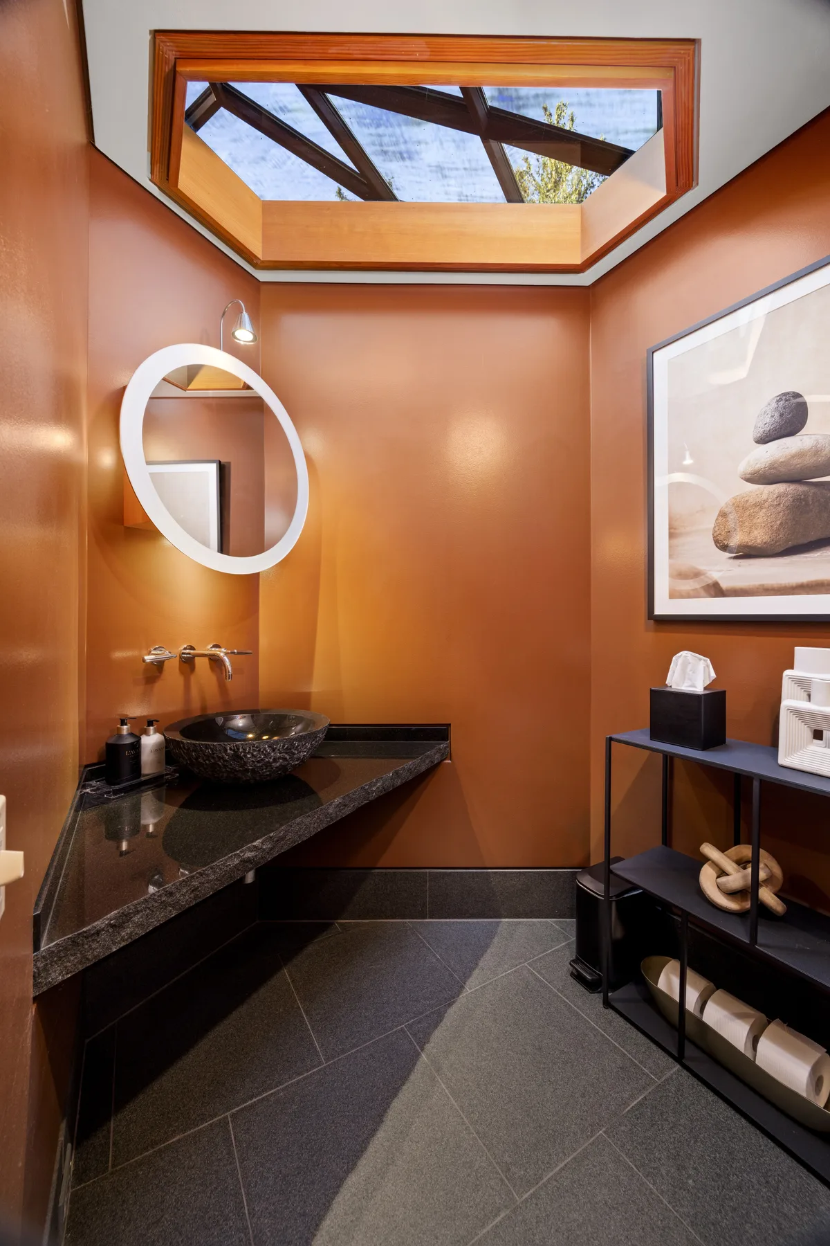 A warm-toned bathroom with a stone sink beneath a skylight.