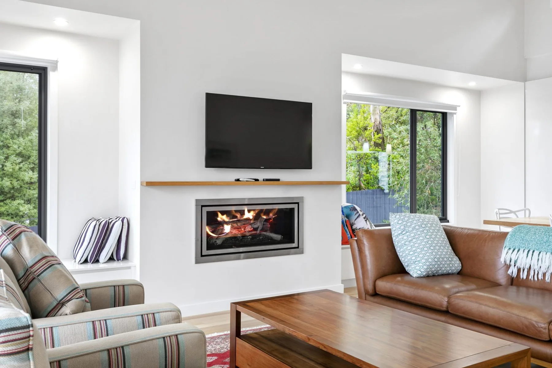 Una sala de estar con un televisor sobre una chimenea y asientos junto a grandes ventanas.