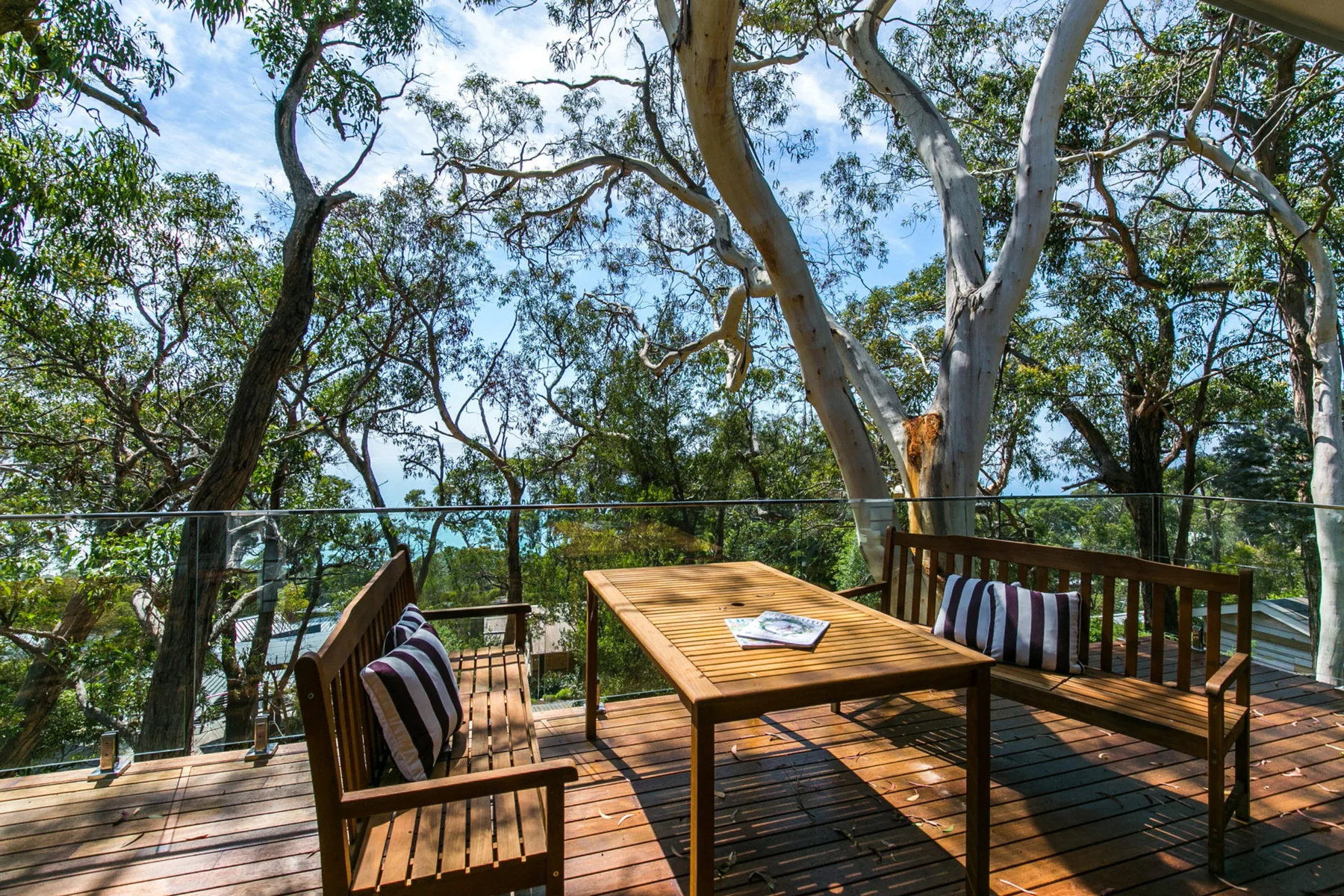 Una terraza de madera con mesa y asientos bajo árboles frondosos.