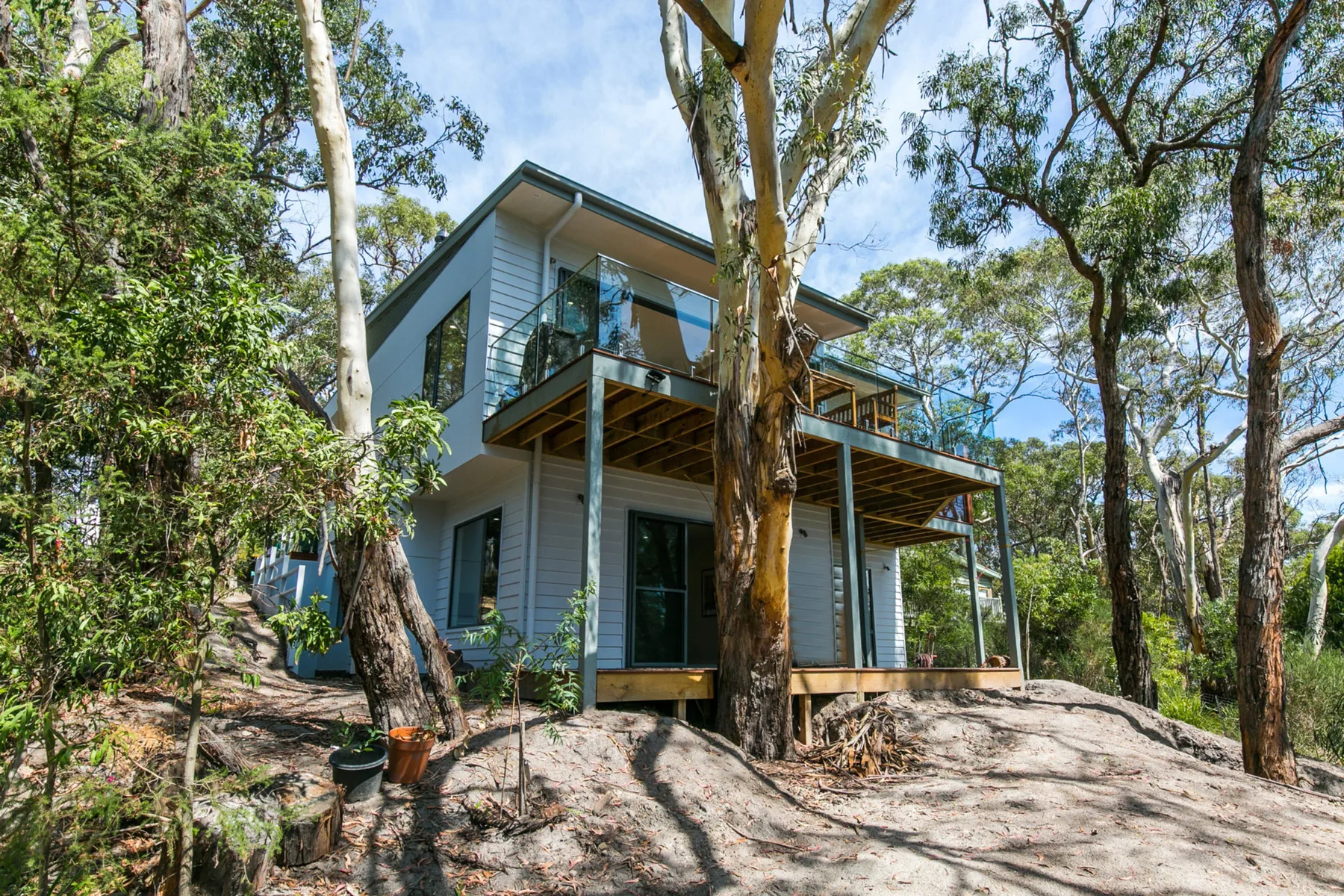 Una casa moderna con una terraza elevada se encuentra entre árboles en una ladera rocosa.