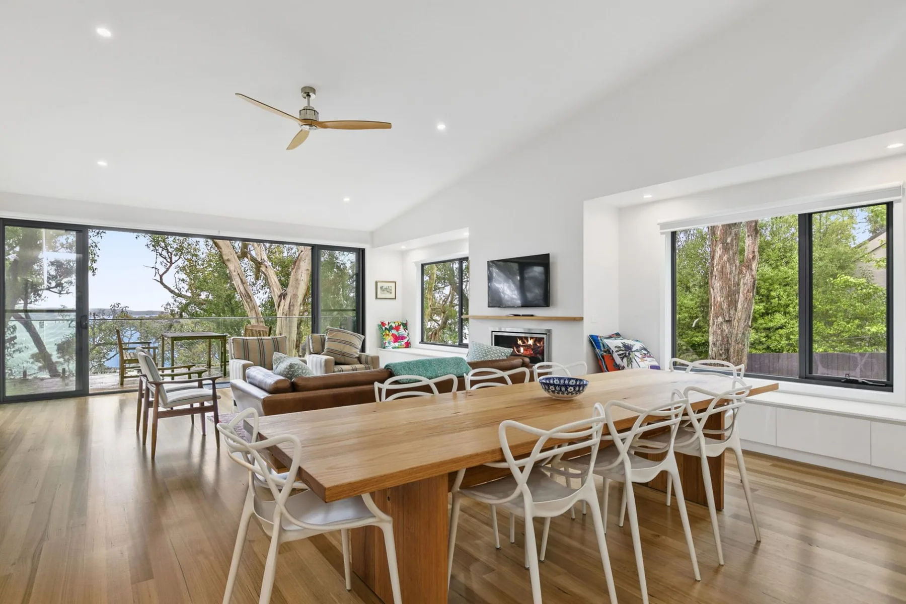 Un comedor y sala de estar diáfanos y luminosos, con una mesa de madera y ventanales.