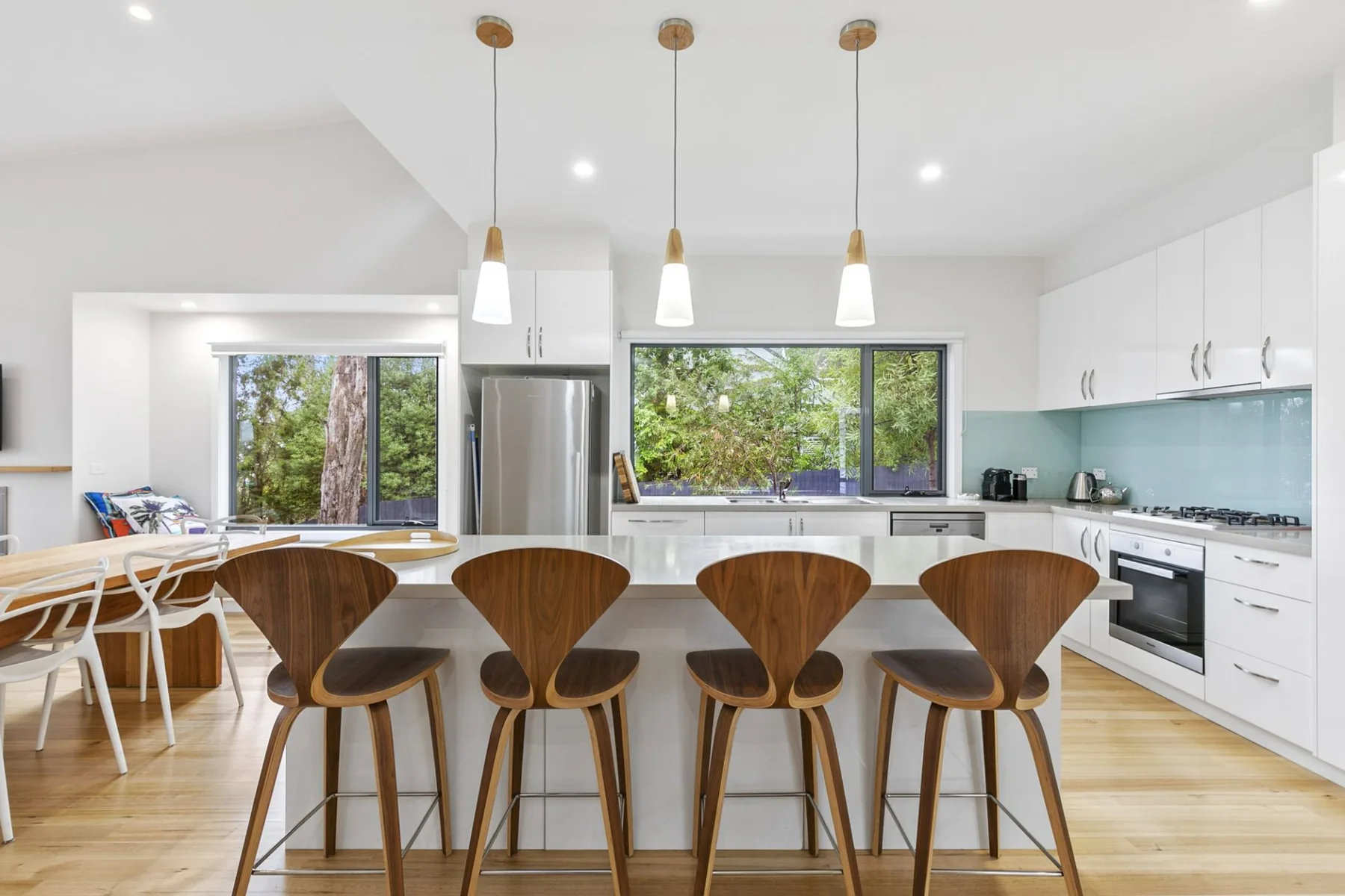 Una cocina luminosa con una isla larga y taburetes de madera bajo luces colgantes.