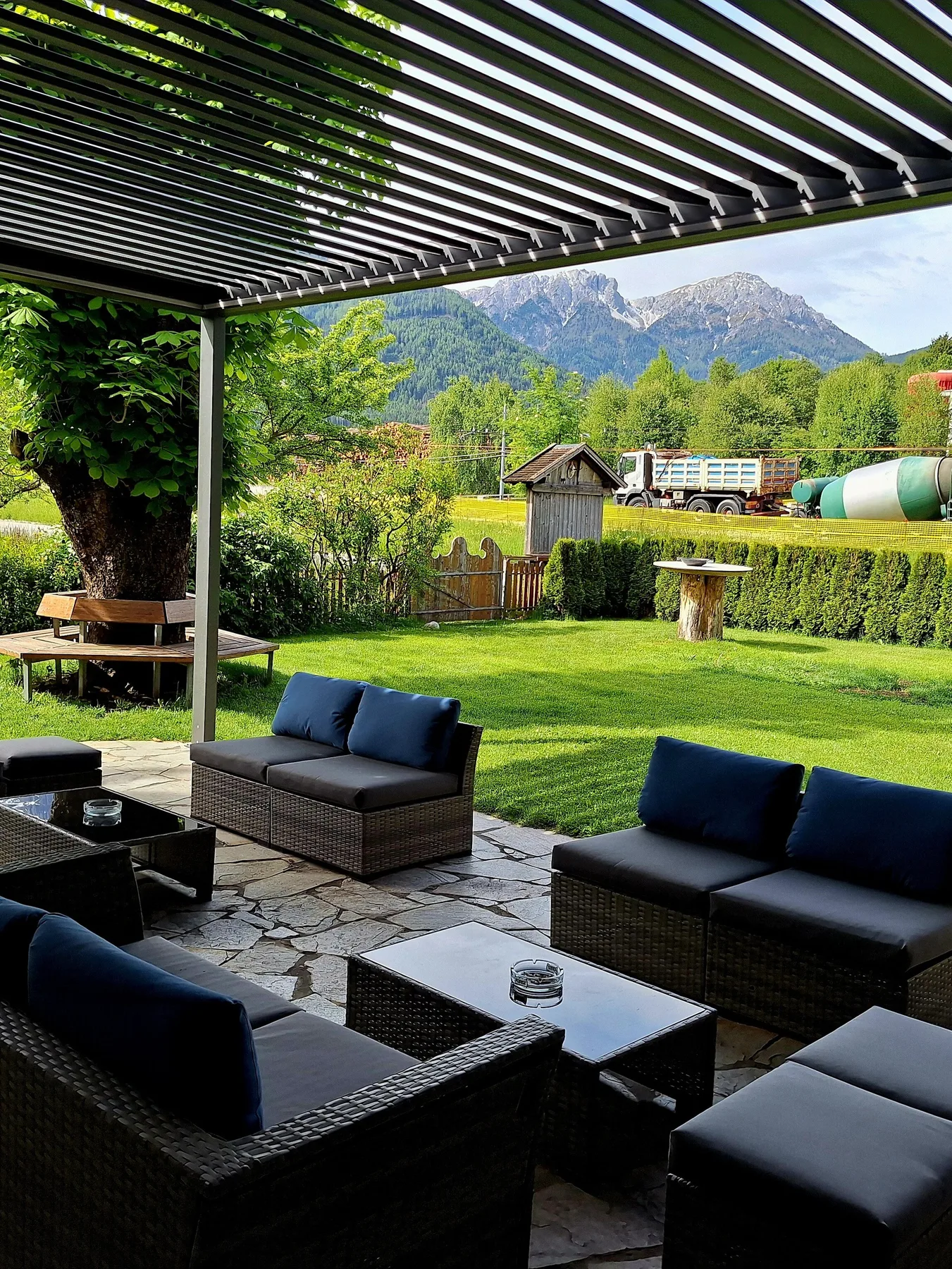 Representative hotel space: A covered patio with dark seating overlooks a green garden and mountain scenery.