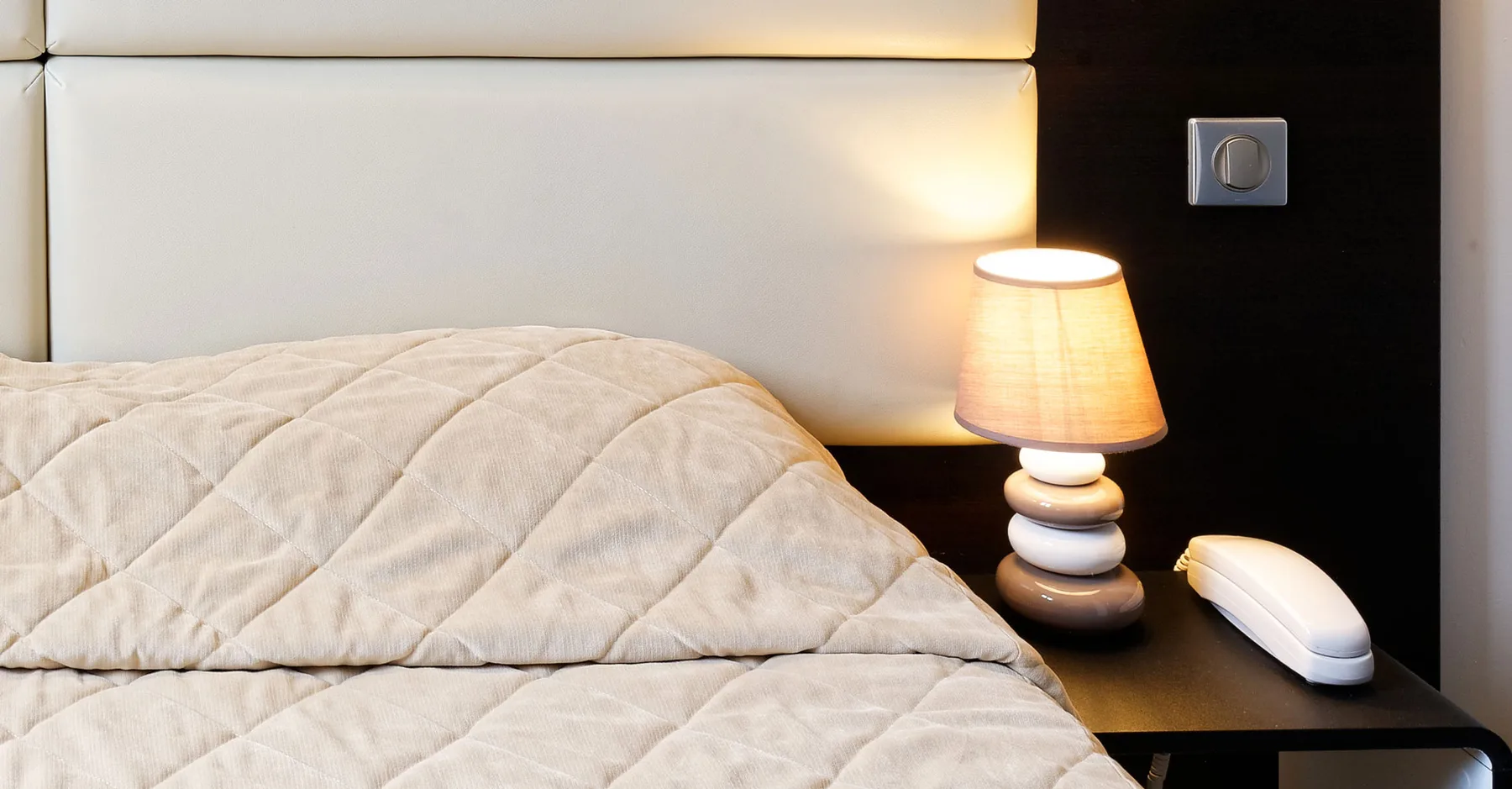 Espacio representativo del hotel: Un dormitorio con una cama bien hecha y una lámpara de noche encendida.