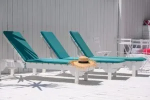 Representative hotel space: Outdoor poolside seating with teal lounge chairs beside a white fence.
