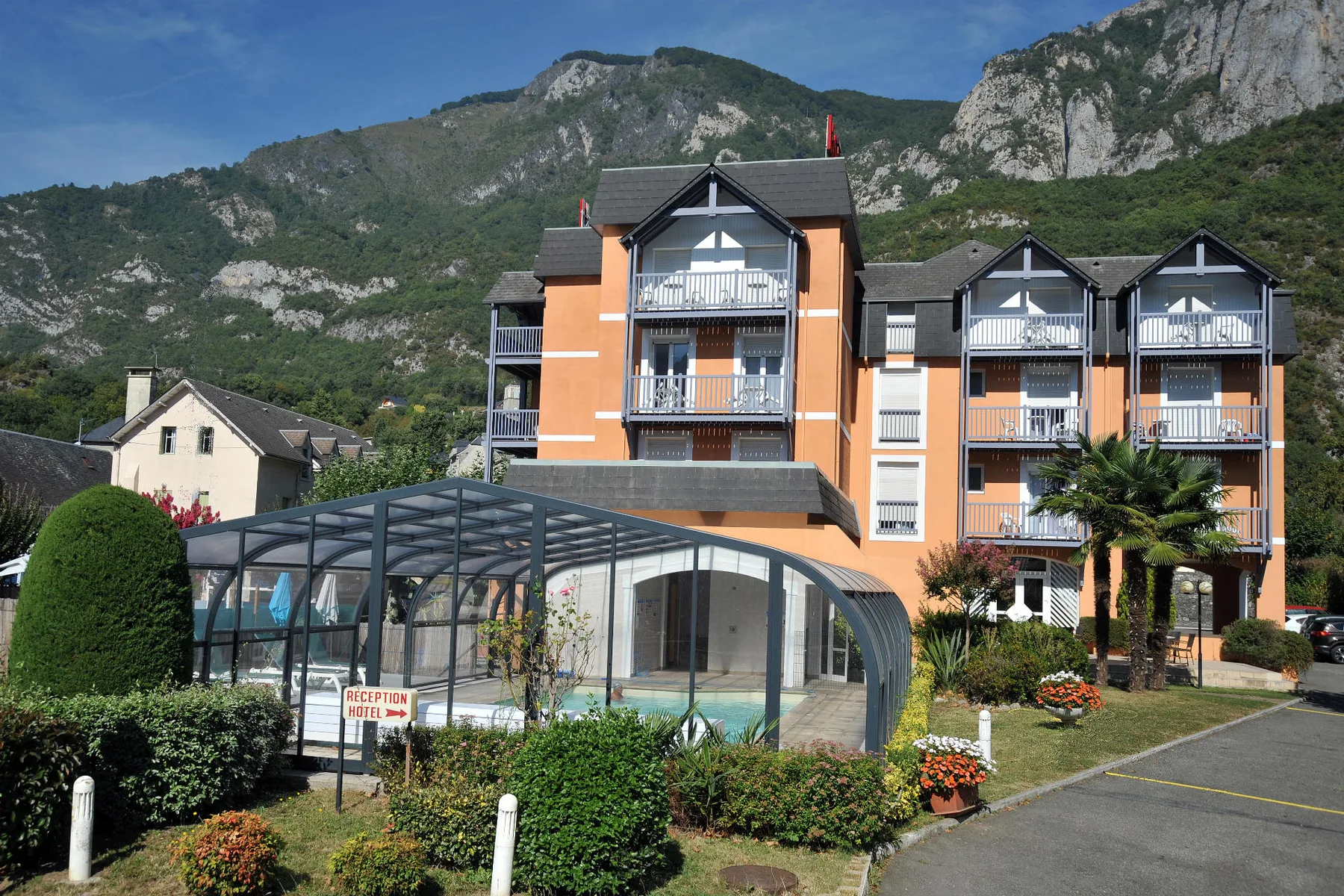Espacio representativo del hotel: Un edificio hotelero con balcones se alza junto a una zona de piscina cubierta en un entorno montañoso.