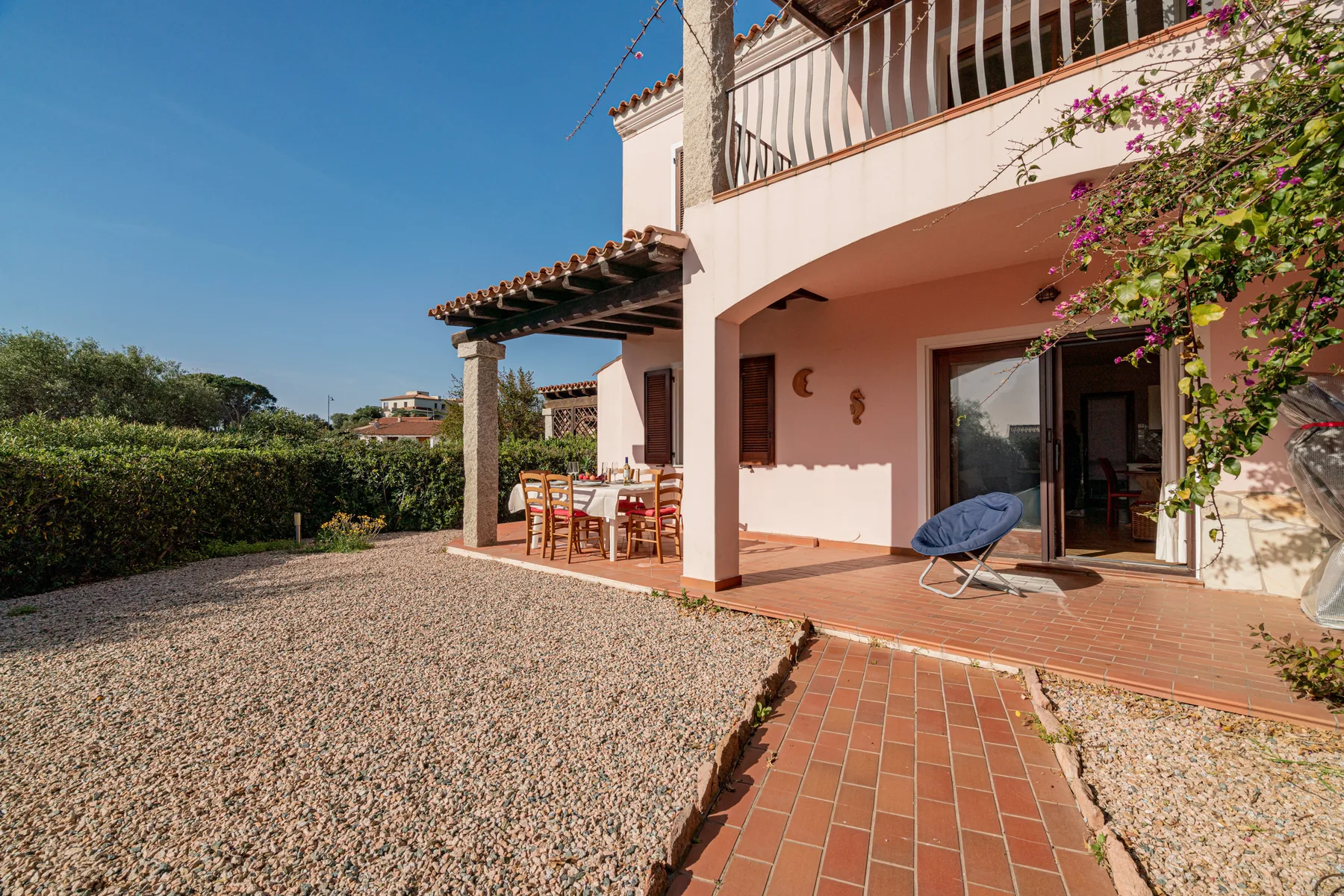 Un patio soleado junto a una casa rosa da a un jardín de grava.