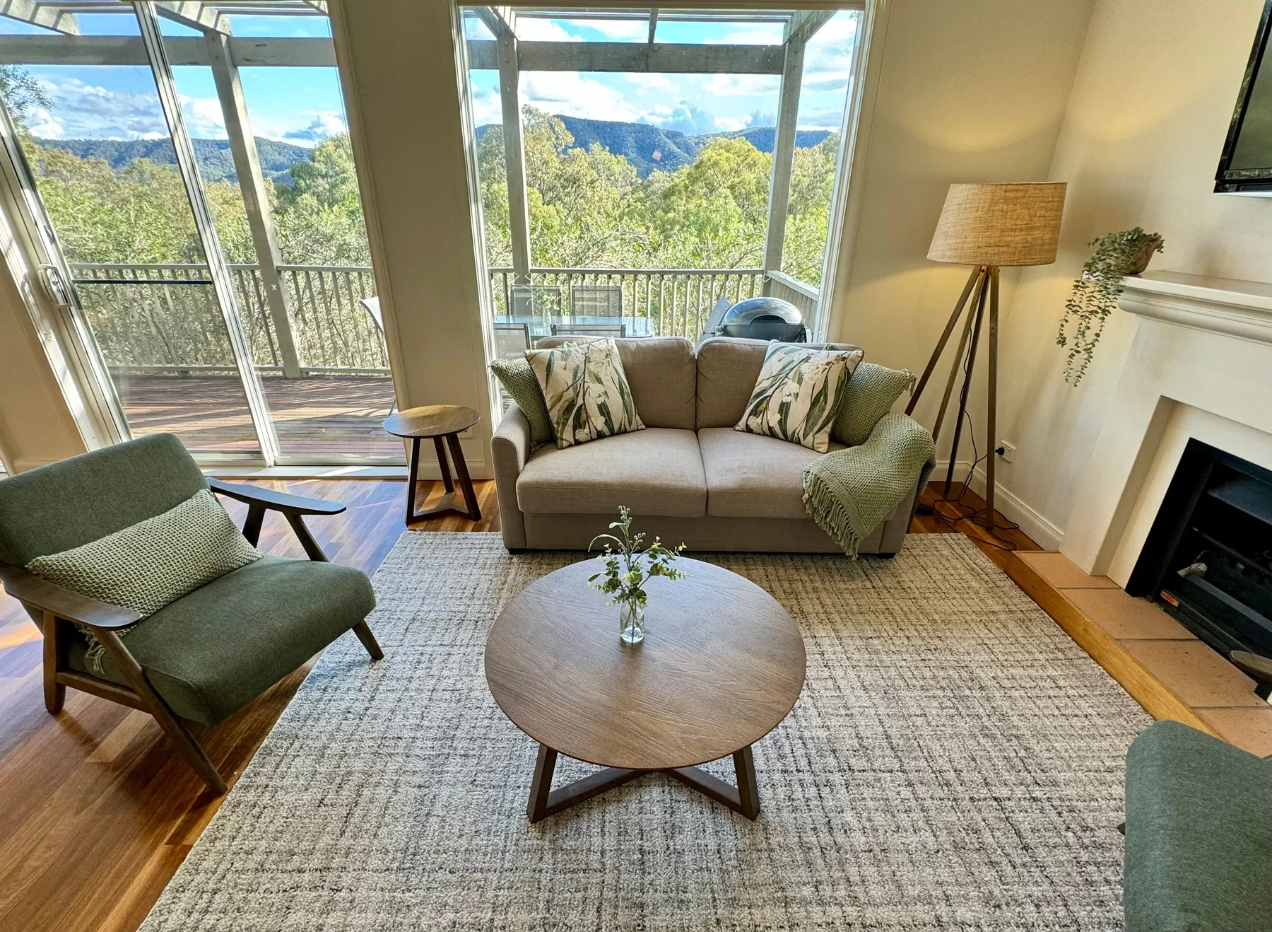 Una sala de estar con asientos y una mesa de centro junto a grandes ventanas con vista a un paisaje boscoso.