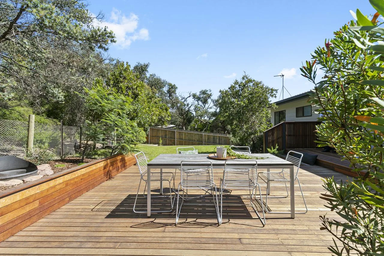 Una zona de comedor al aire libre en una terraza de madera, rodeada de vegetación.
