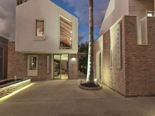 Espacio representativo del hotel: La entrada de un edificio moderno da a un patio pavimentado con una palmera en el centro.