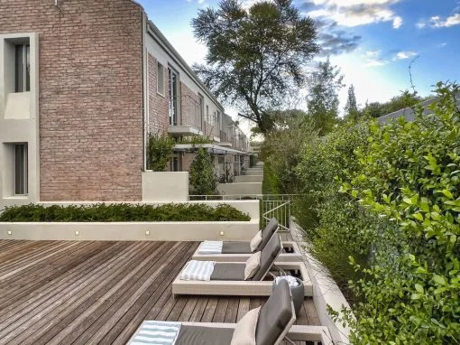 Espacio representativo del hotel: Una terraza exterior con asientos acolchados junto a un seto y un edificio moderno.