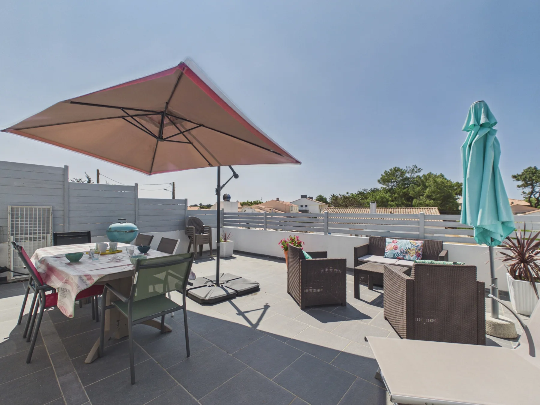 A sunny rooftop terrace with outdoor seating, a dining table, and large umbrellas.