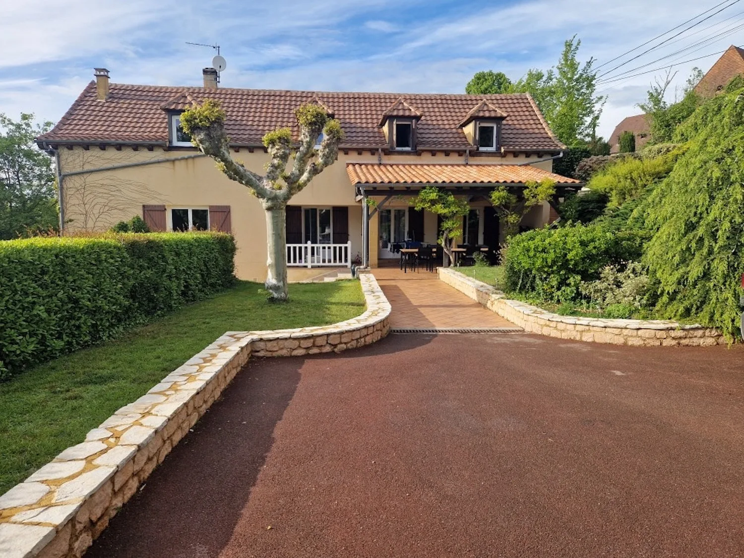 Una casa con entrada pavimentada, jardín y patio cubierto.