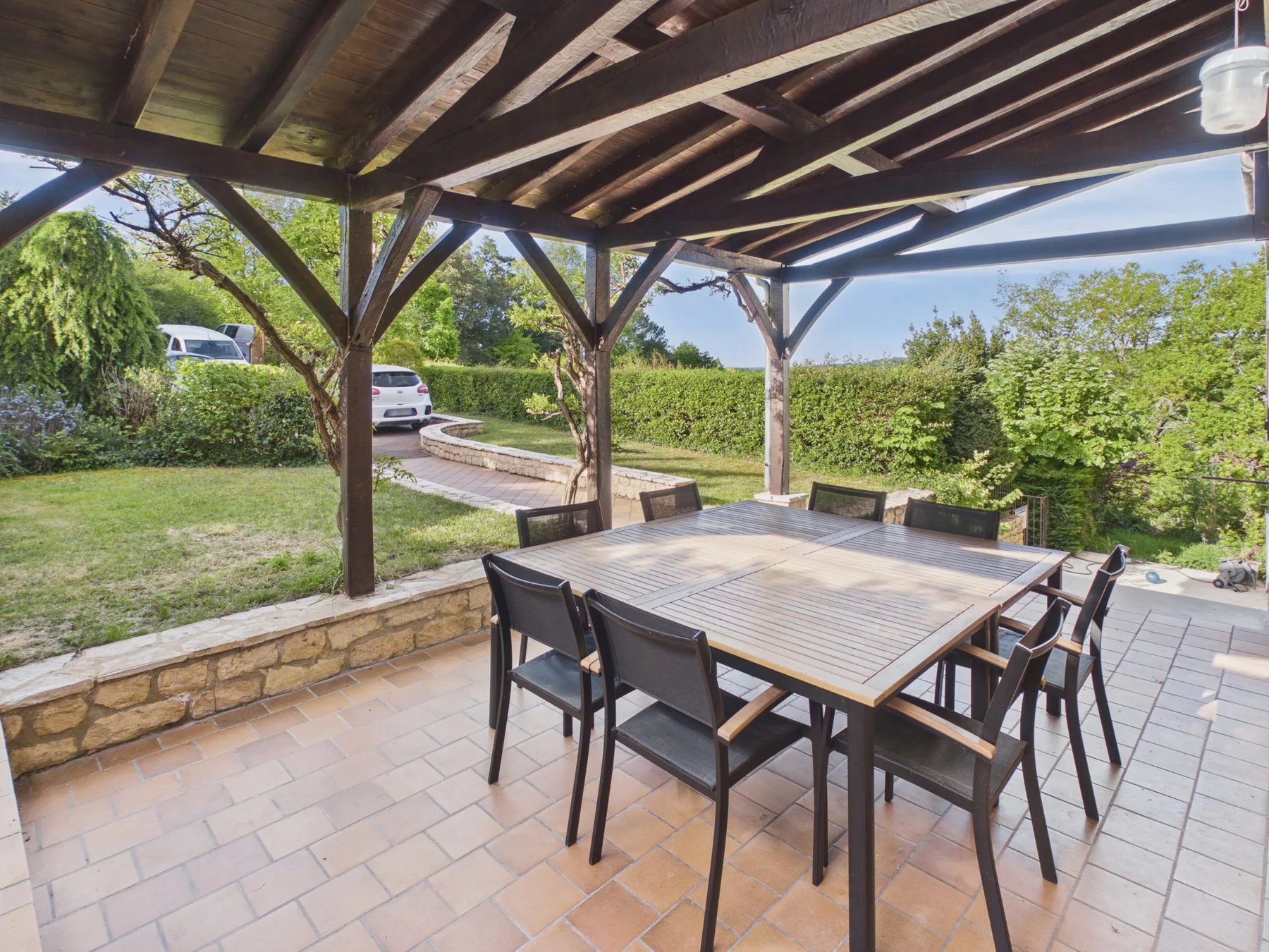 Comedor en un patio cubierto con mesa y sillas junto a un jardín.