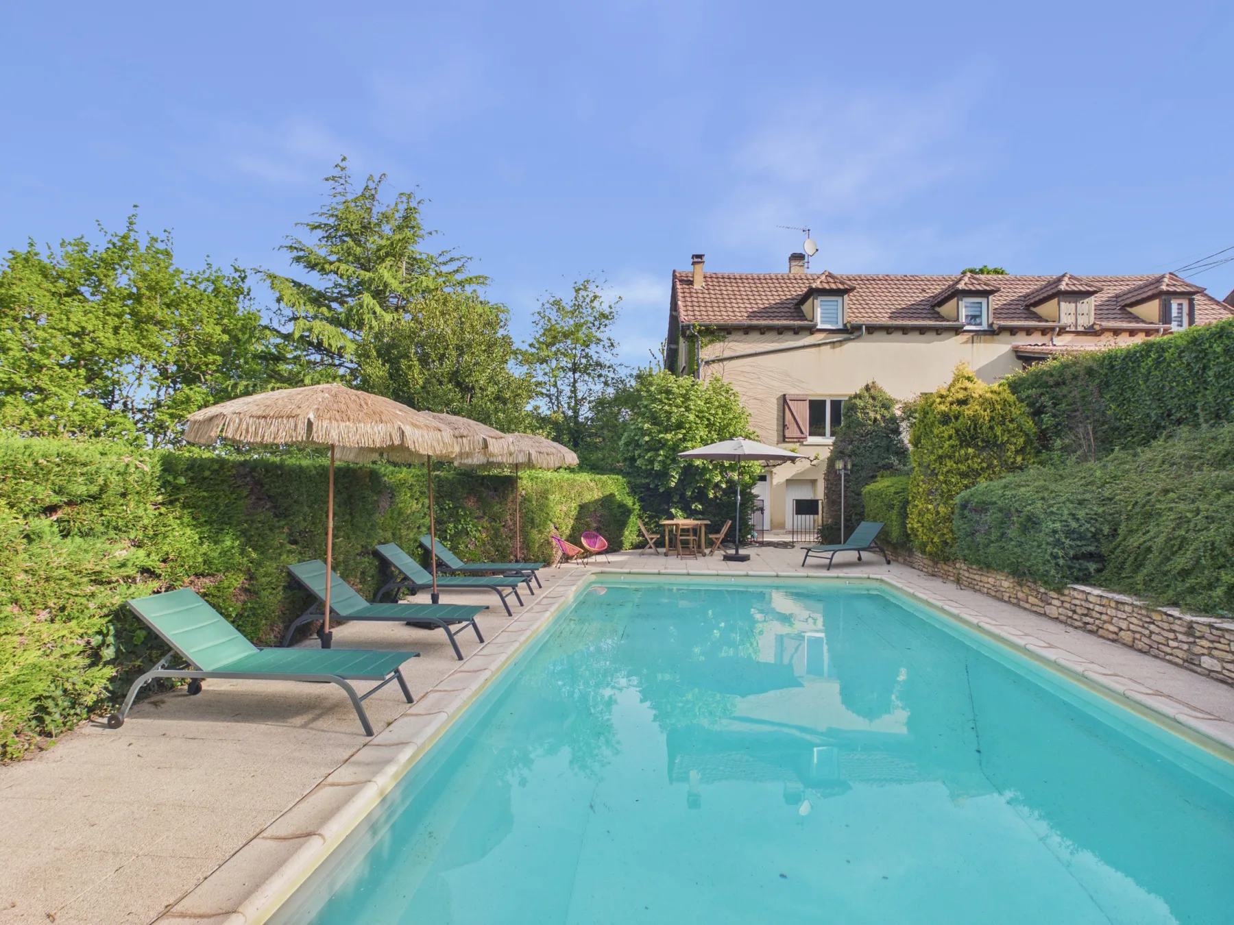 Una piscina está junto a asientos reclinables y un jardín con vegetación.