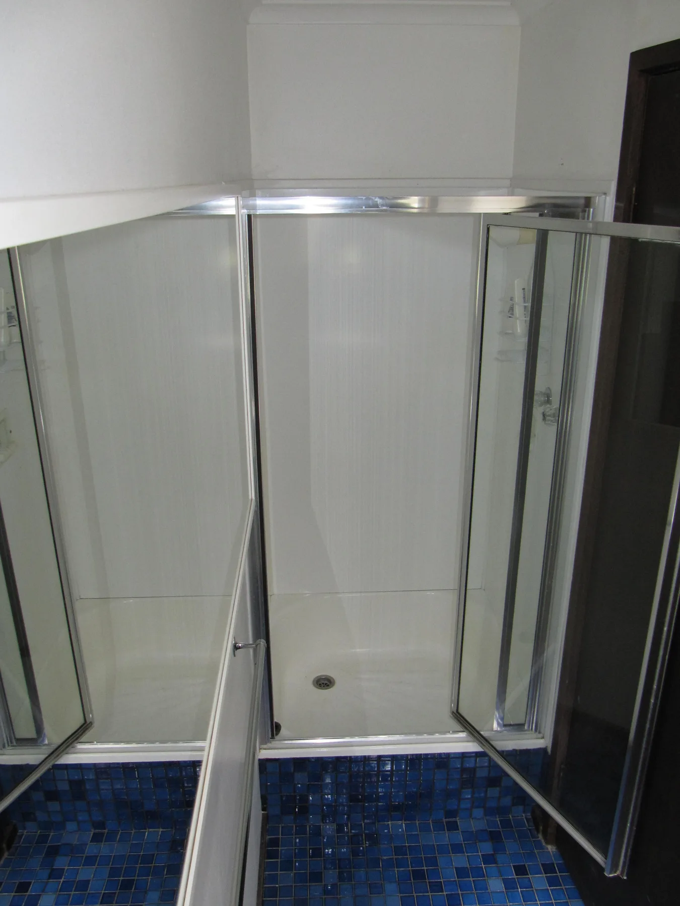 A glass shower enclosure stands above a blue tiled floor.