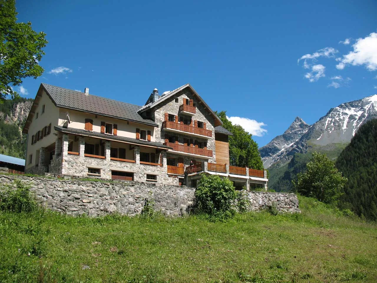 Espacio representativo del hotel: Un alojamiento de montaña se alza sobre una pendiente cubierta de hierba bajo un cielo azul despejado.