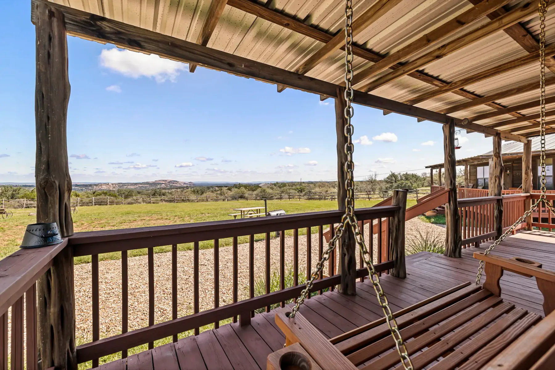 A covered wooden deck overlooks open fields and a distant landscape.