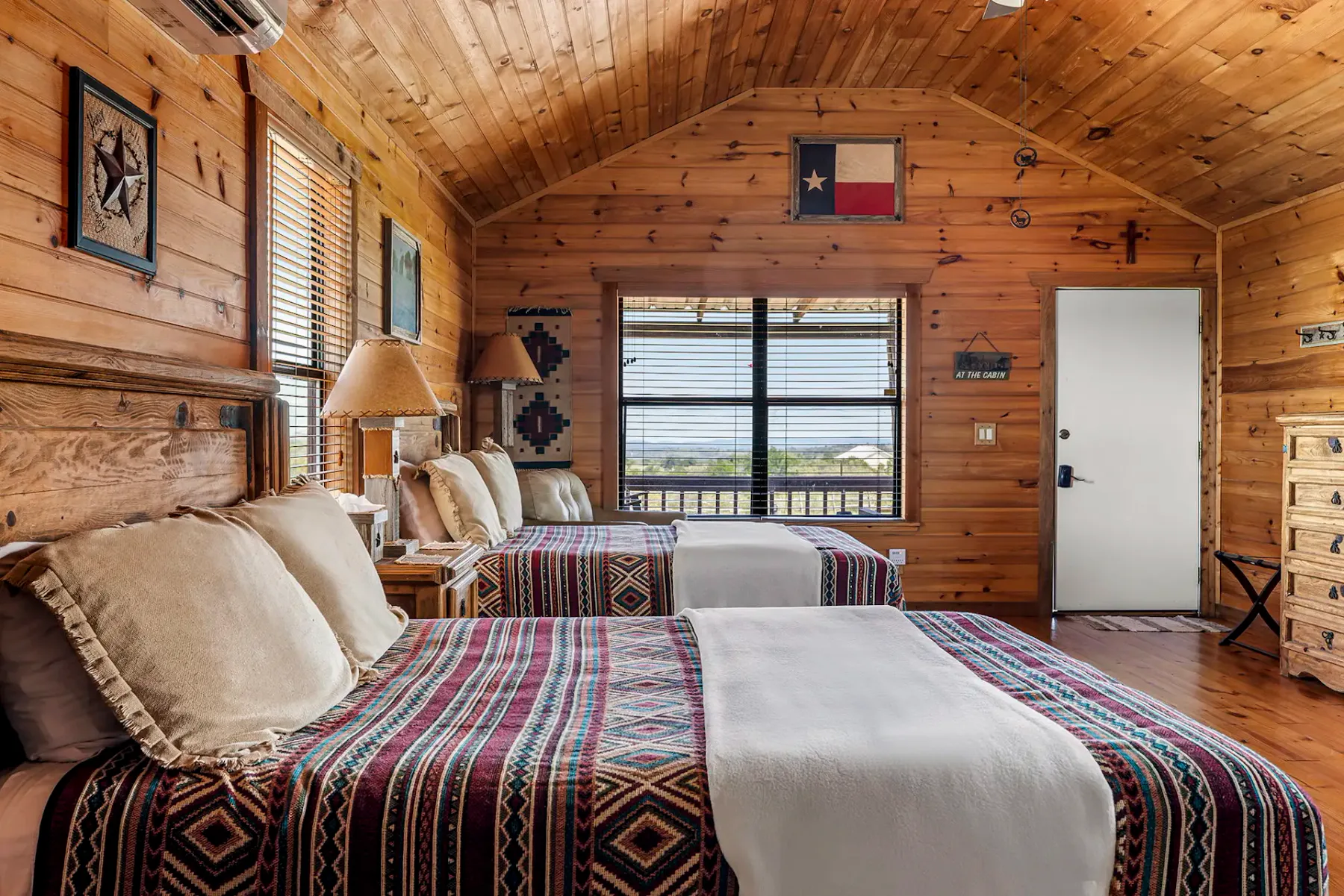 A wood-paneled bedroom with patterned bedding and a window overlooking the landscape.