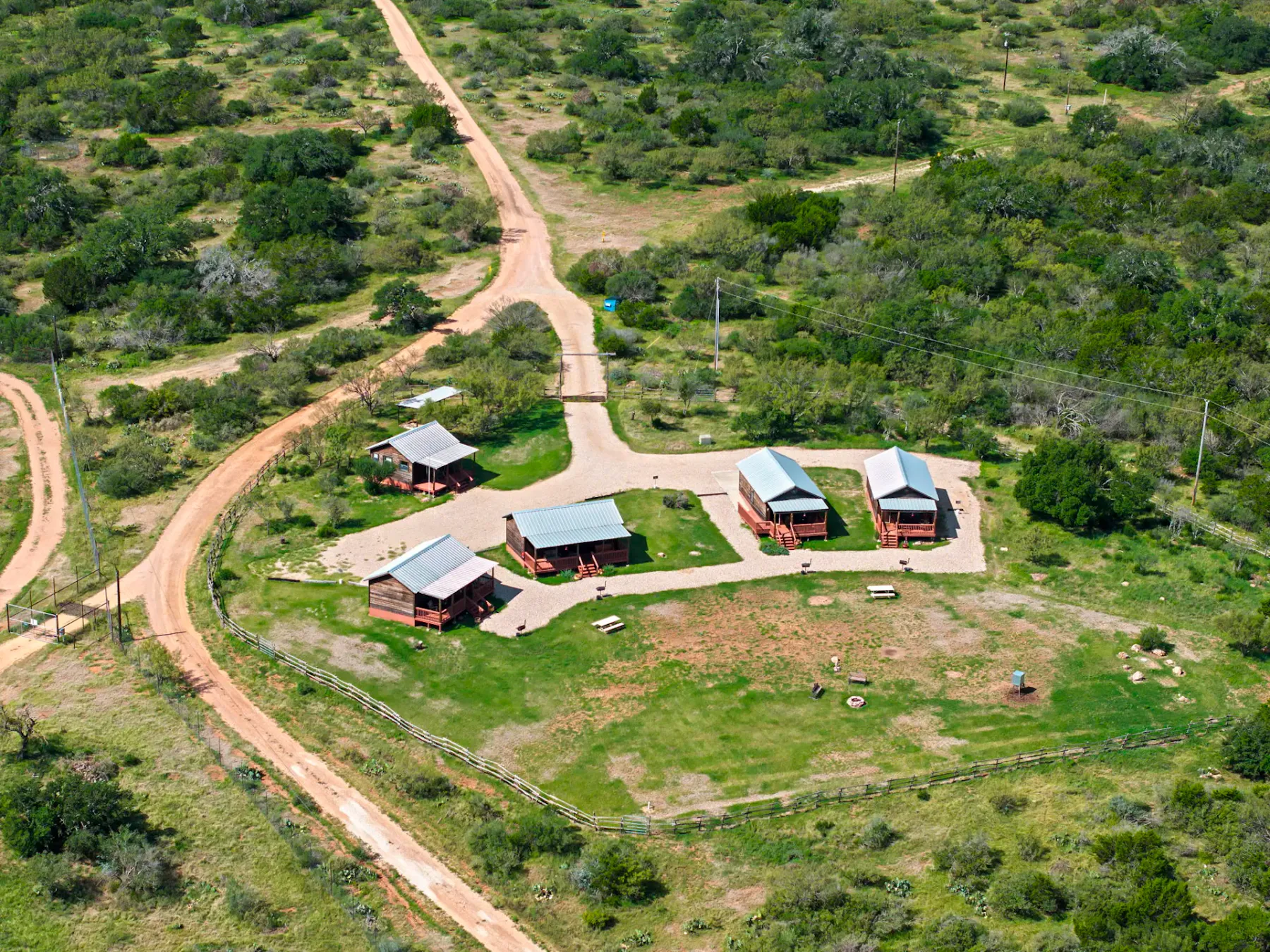 Shared amenity: Aerial view of several cabins beside winding dirt roads in a green landscape.