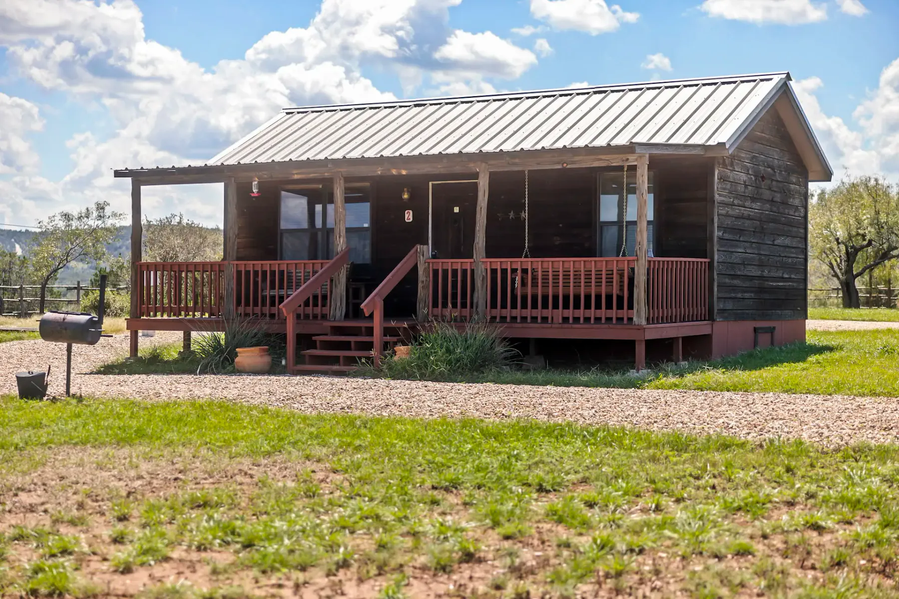 A small cabin with a covered porch stands beside a gravel drive.
