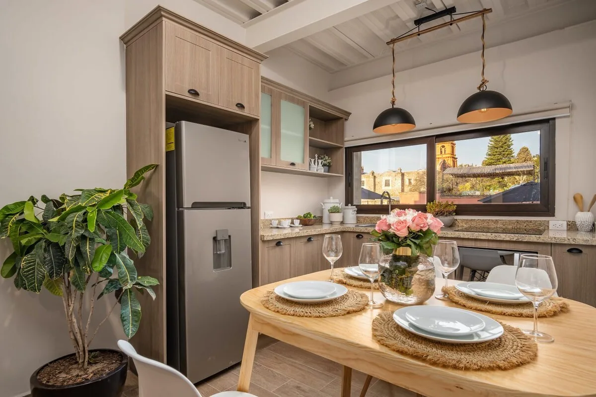 A dining area with a set table, pendant lights, and a wide window.